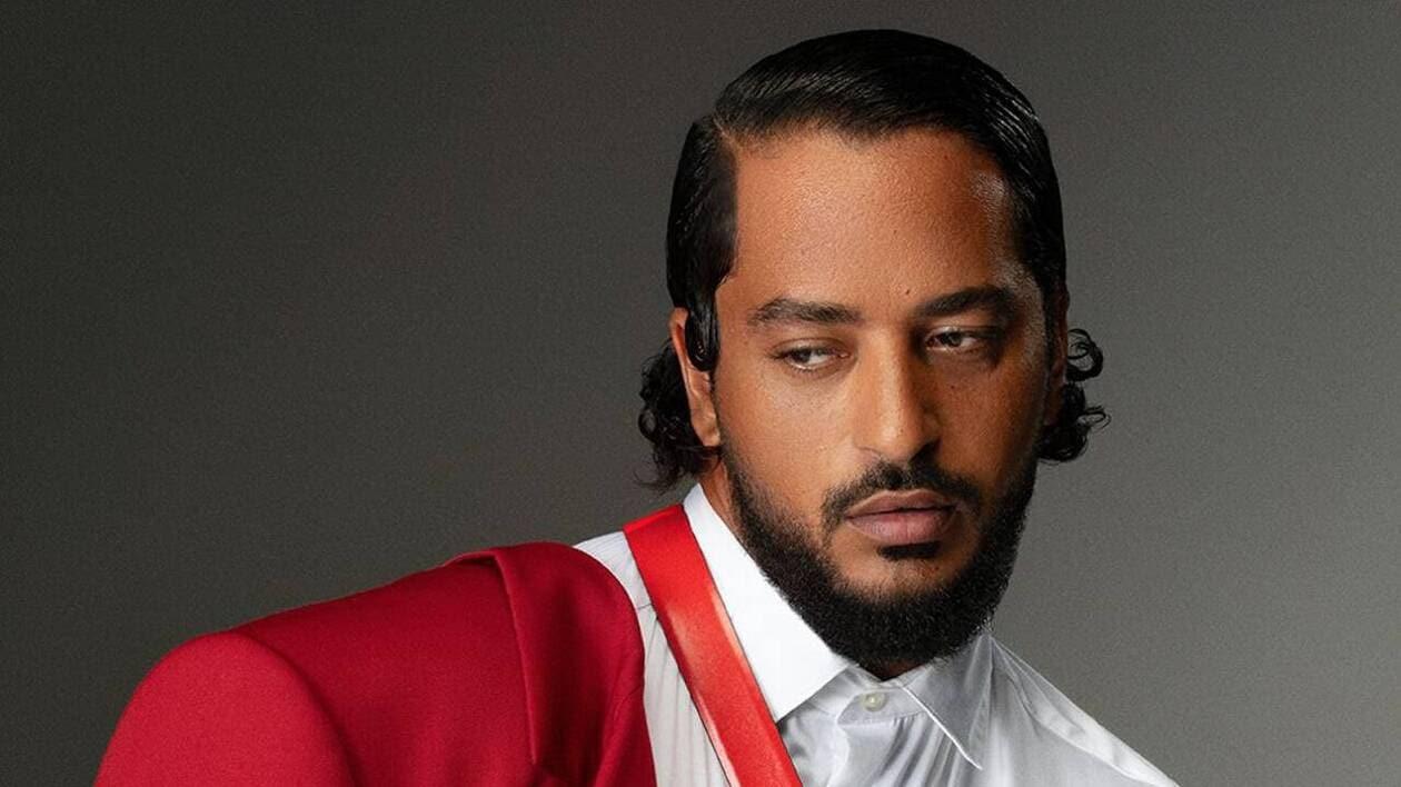 Le chanteur Slimane qui porte une chemise blanche et une veste rouge.