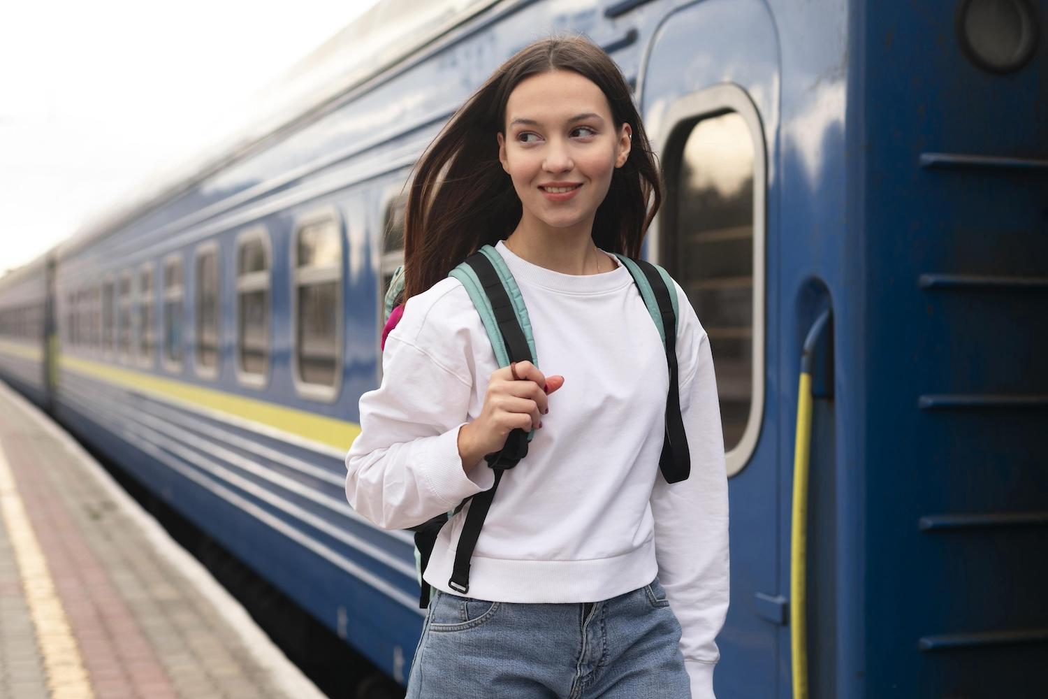 Une jeune étudiante avec un sac à dos est devant un train. 