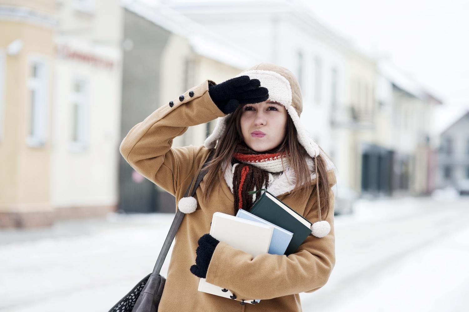 Une jeune étudiante est dehors dans la rue enneigée en habits d'hiver.