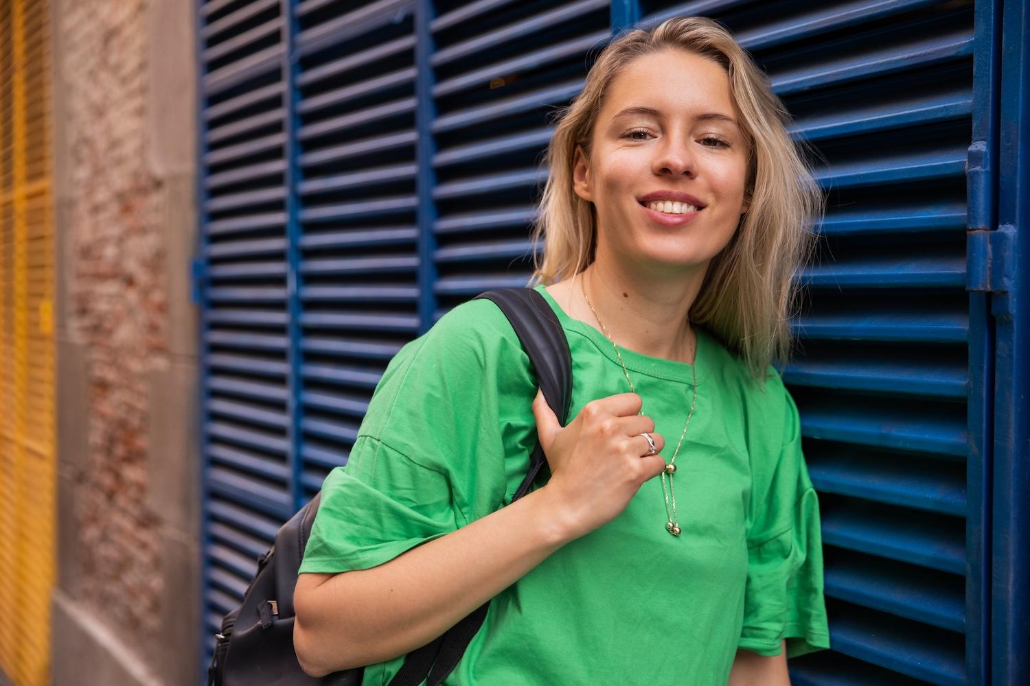 Une jeune femme porte un sac à dos et est souriante.