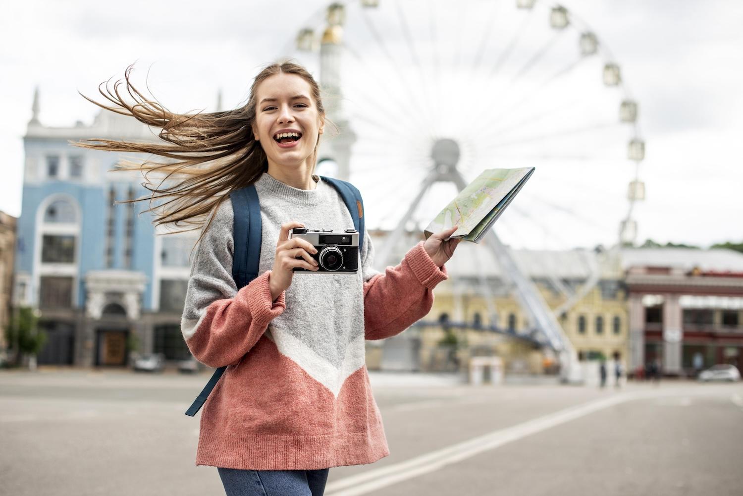 Une jeune femme tient un appareil photo dans une main et un carnet dans l'autre.