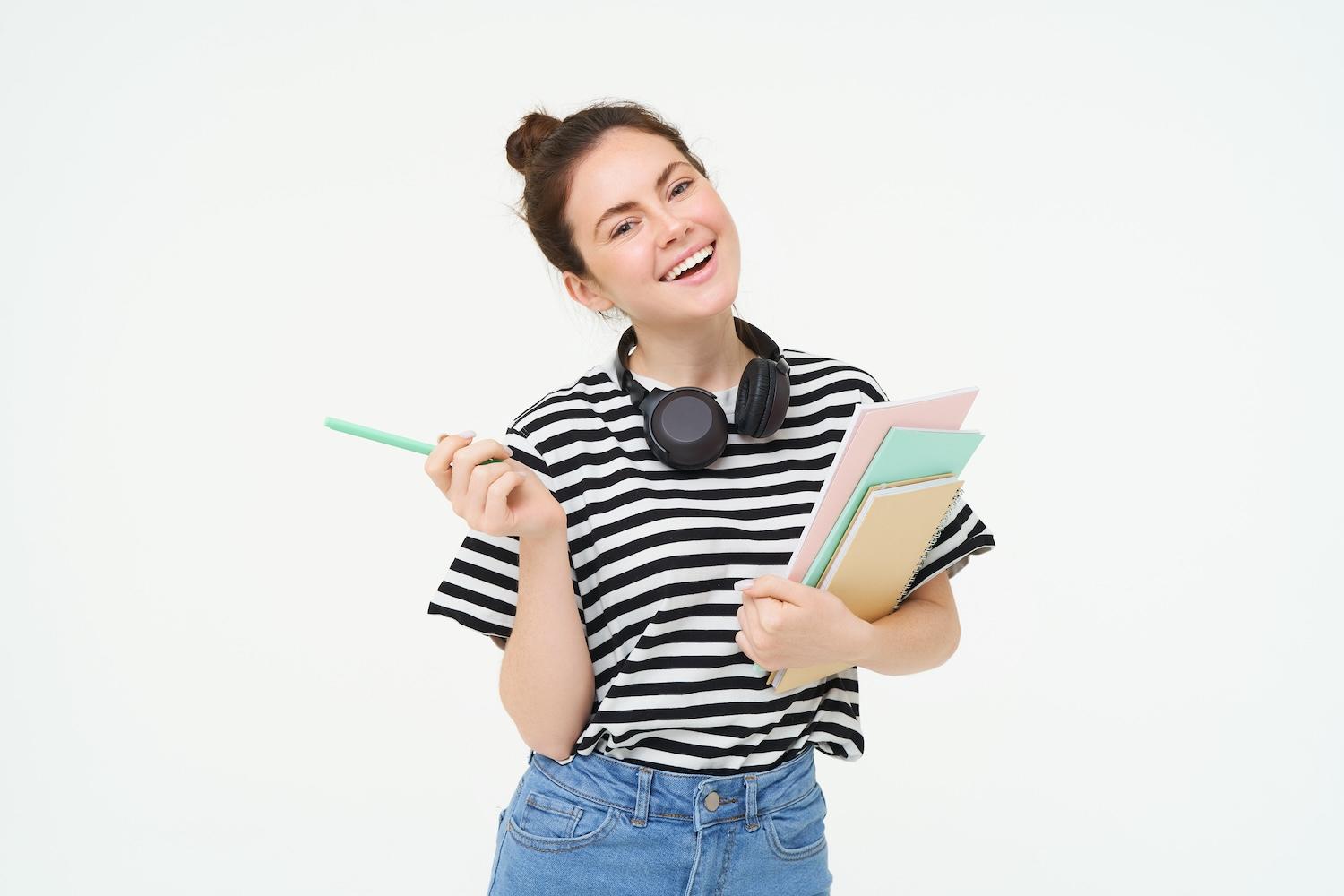 Une jeune étudiante avec un casque autour du cou qui porte des dossiers.