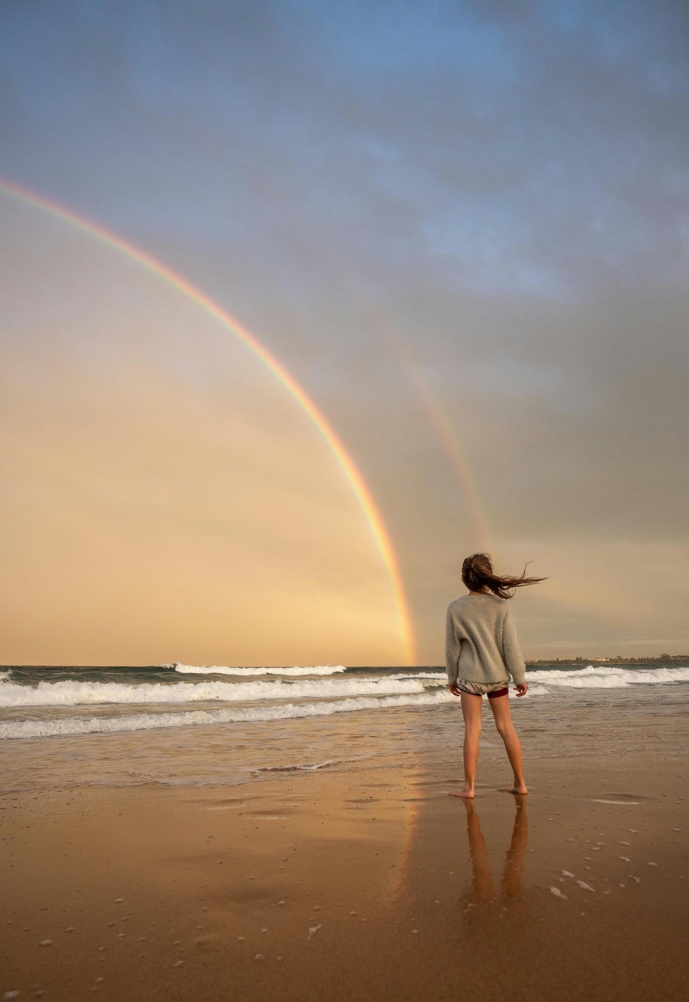 Une femme sur la plage observant un arc en ciel.