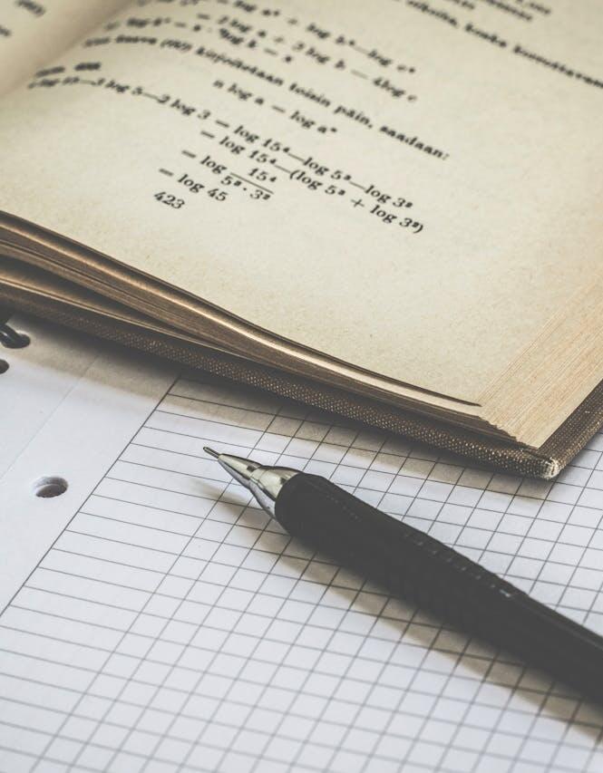 Livre de maths ouvert sur une feuille vierge et avec un stylo noir posé dessus
