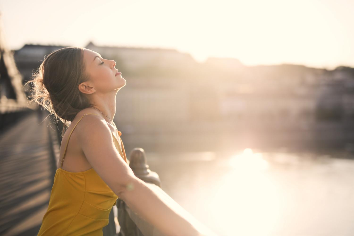 Une jeune femme est sur un pont et ferme les yeux.