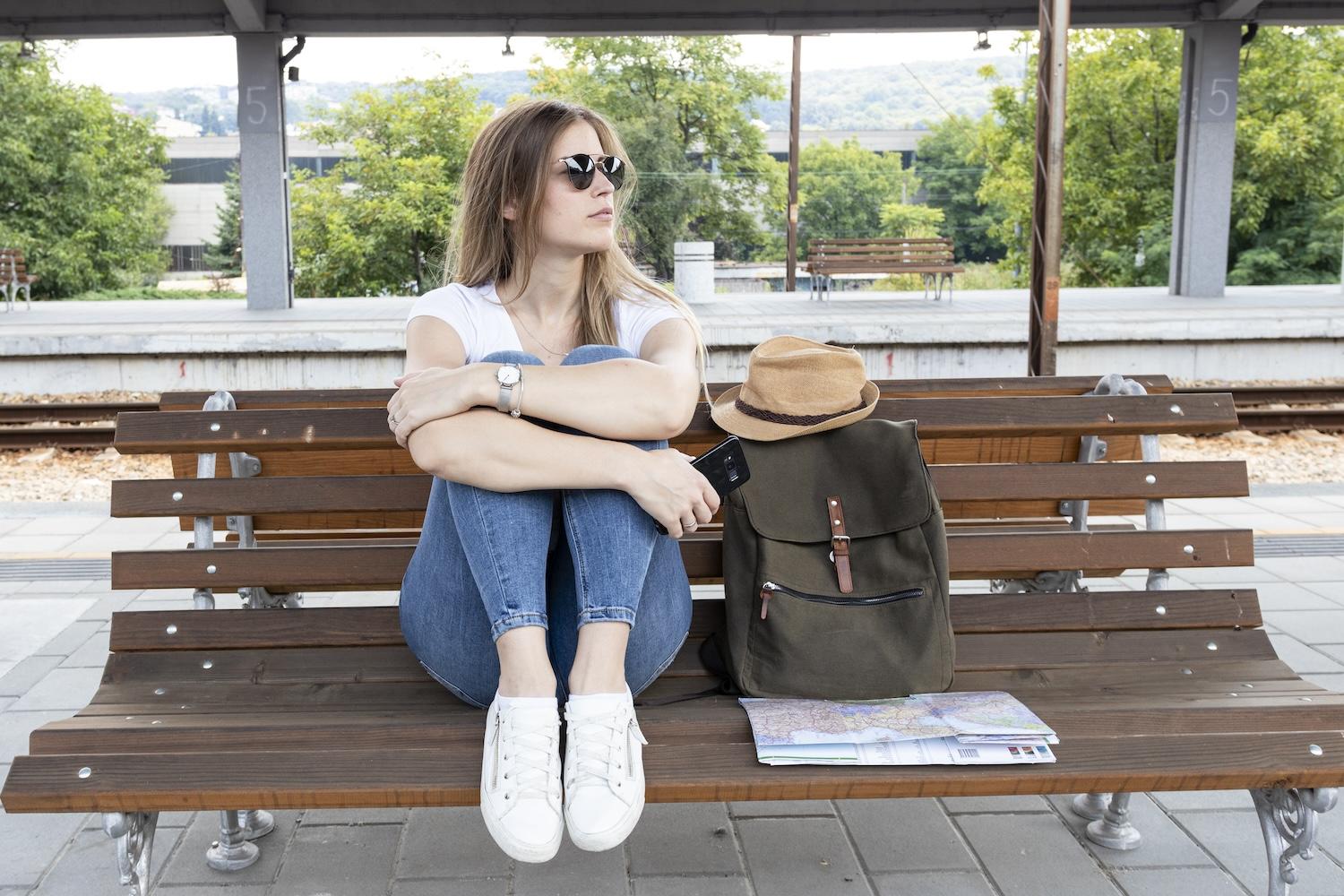 Une jeune femme est assiste sur un banc avec un sac à côté d'elle.