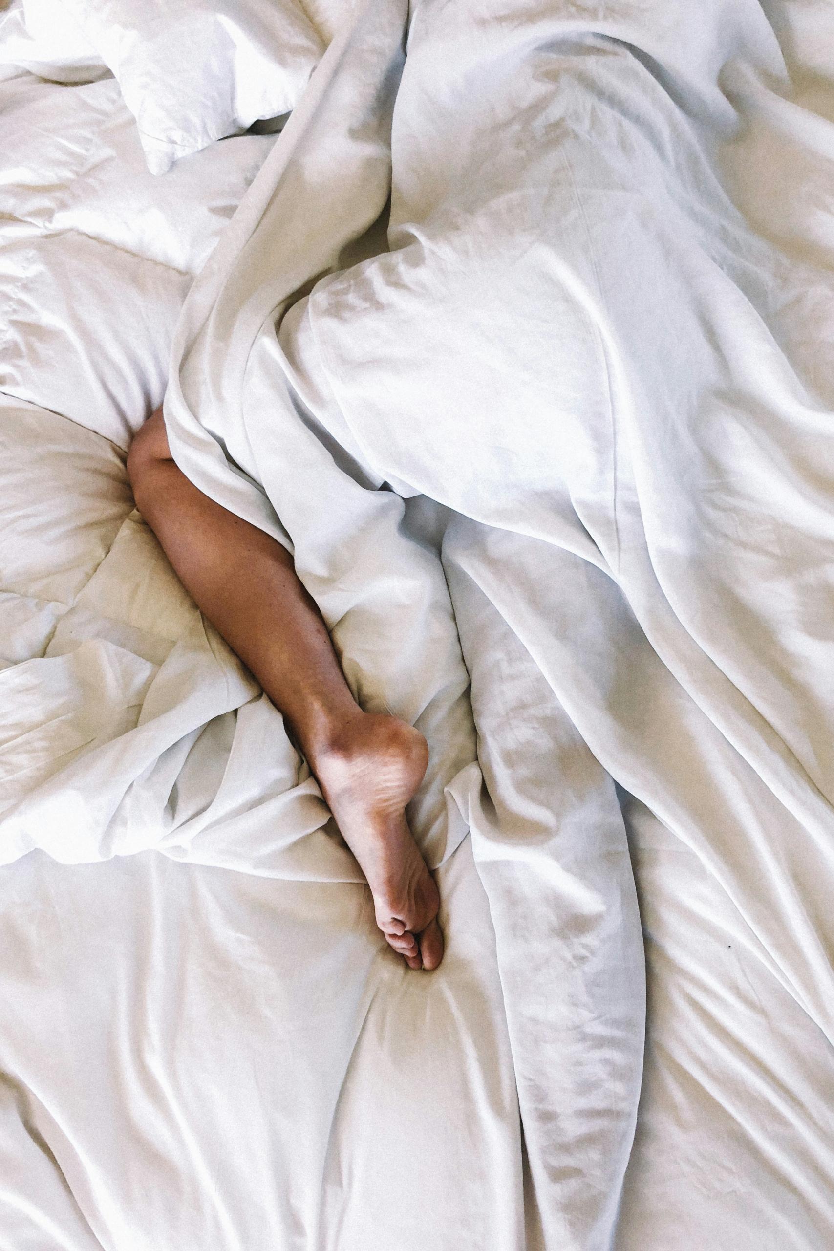 Un pied sort des draps blancs.