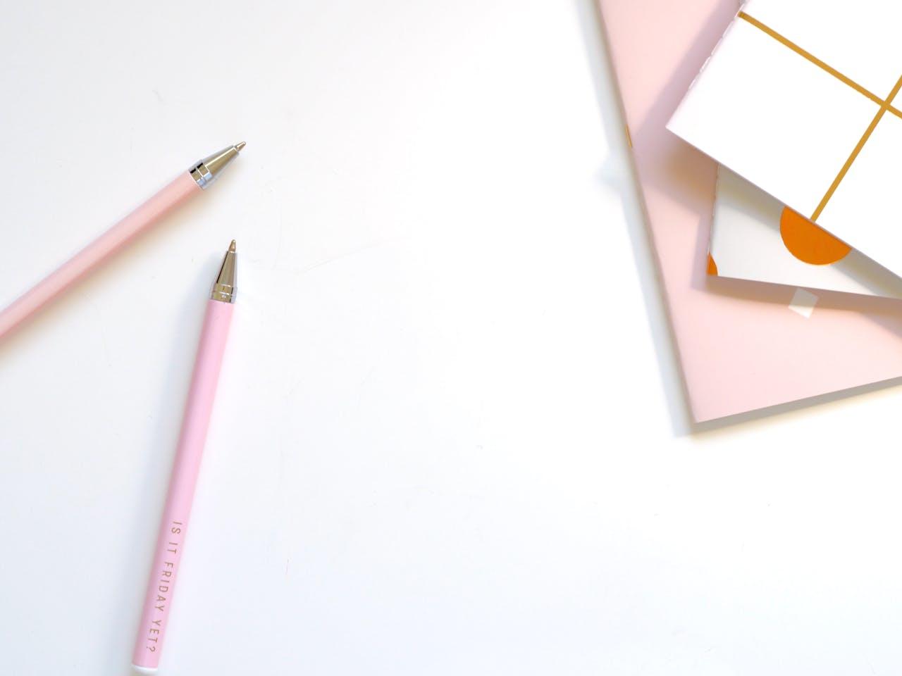 Deux stylos et plusieurs cahiers roses.