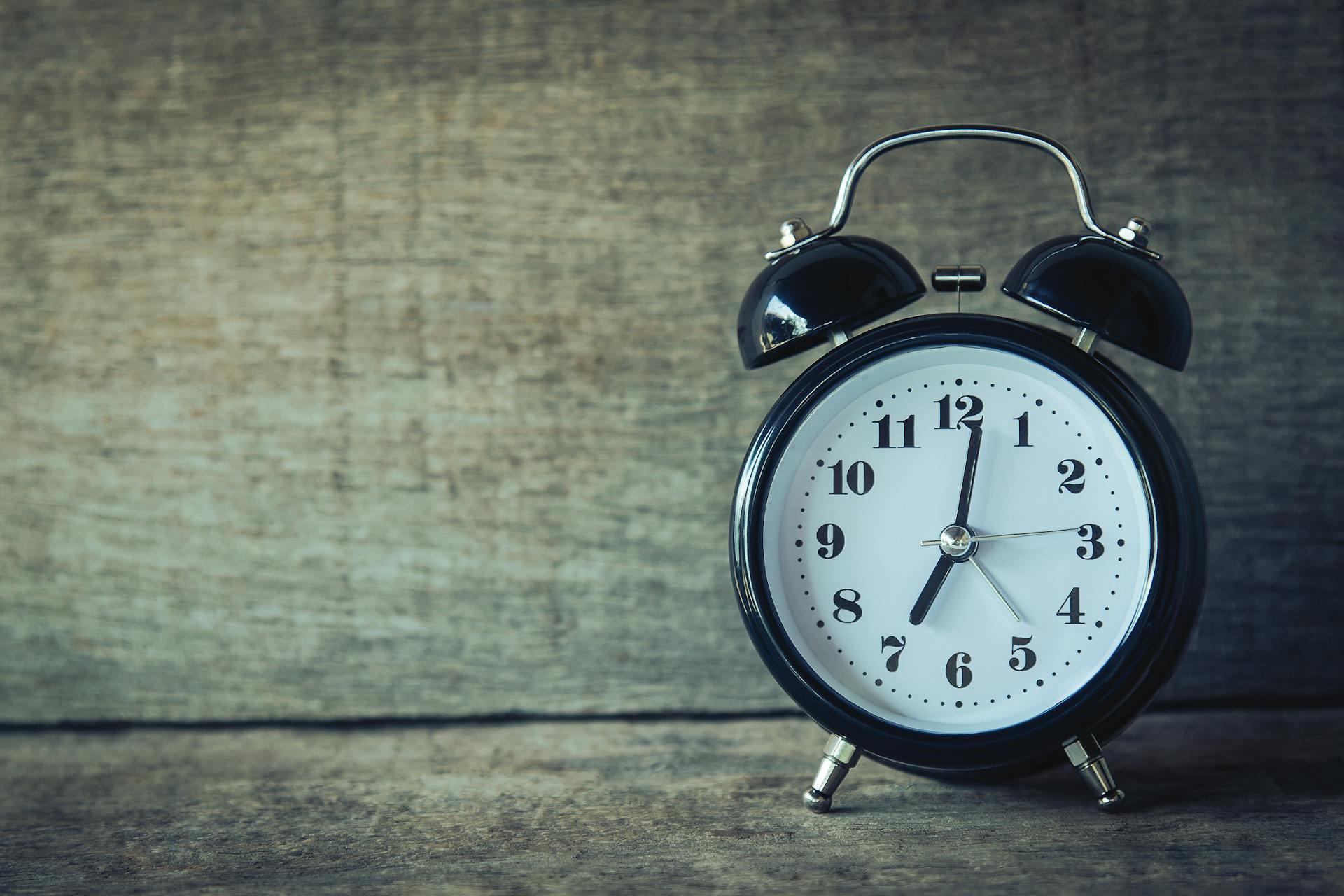 Réveil matin noir posé sur une étagère.