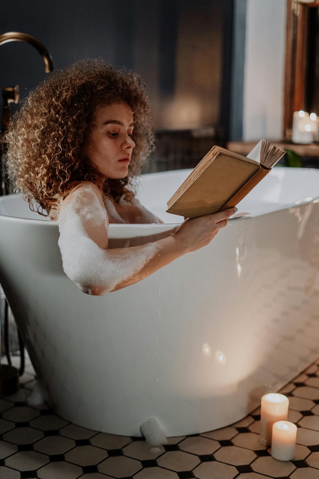 Une jeune femme en train de lire dans son bain.