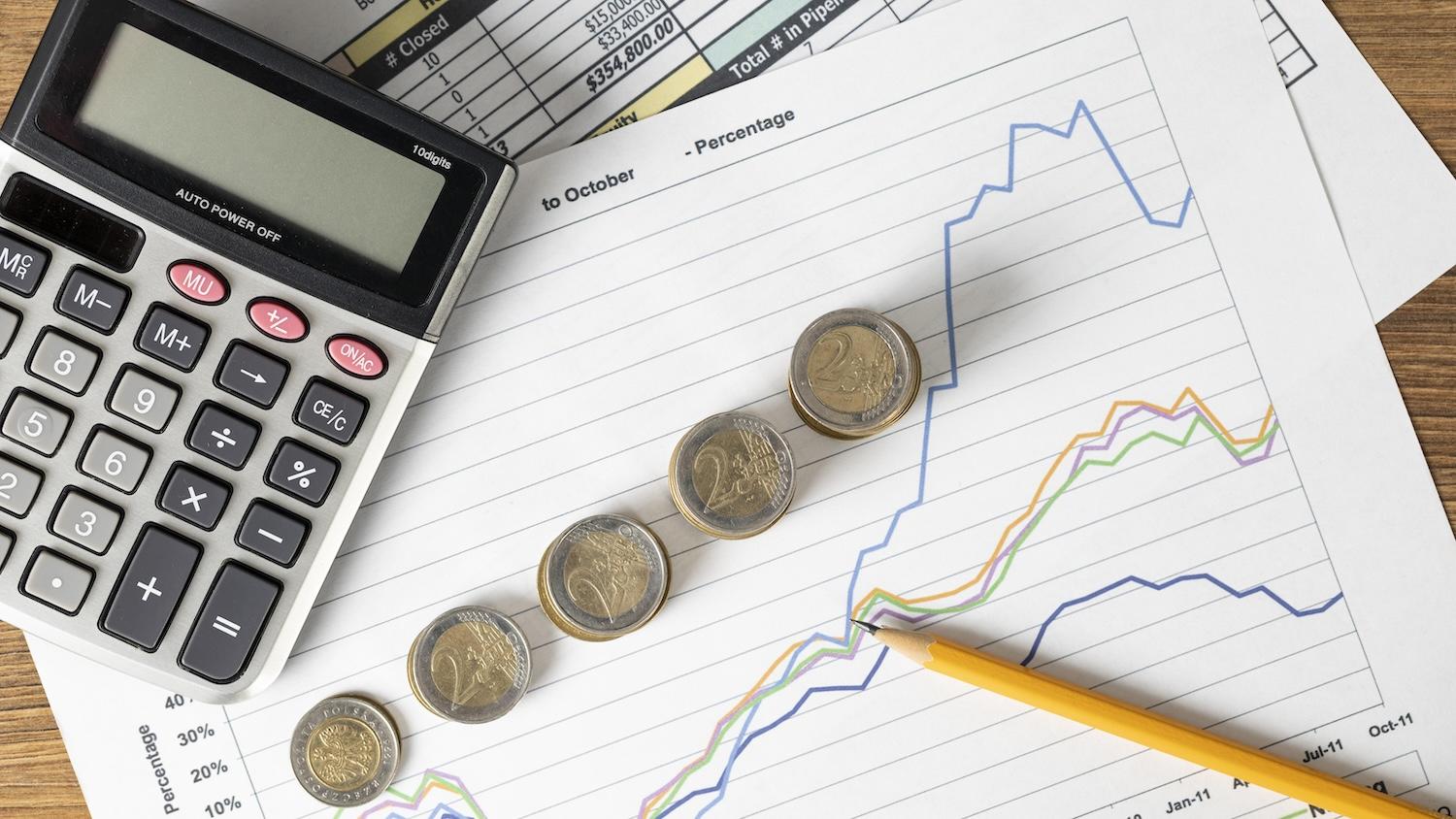 Vue d'une calculette posée sur une table avec des graphiques et des pièces de monnaie.