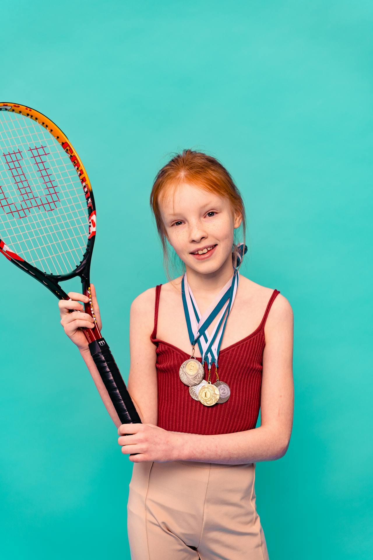 Petite fille rousse tenant une raquette de tennis, le cou décoré de 4 médailles.