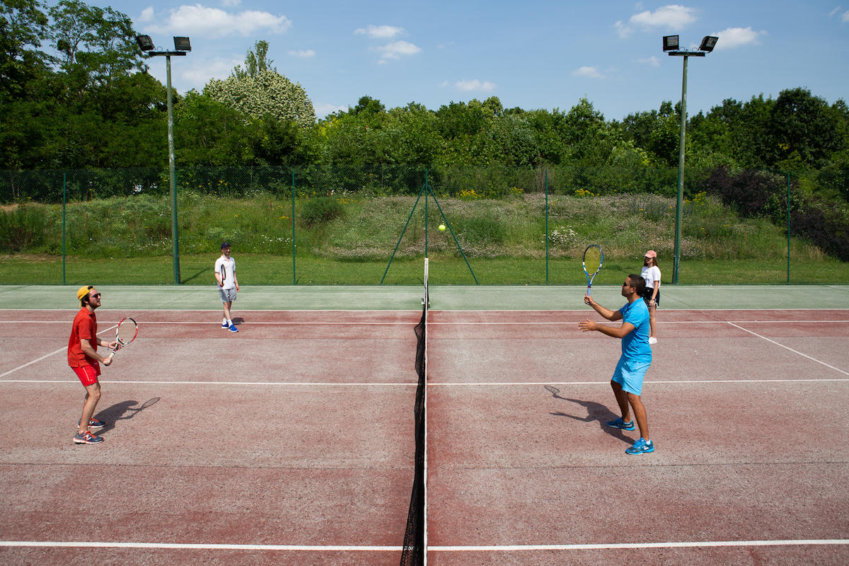 Quatre personnes jouent au tennis sur un court en dur en extérieur.