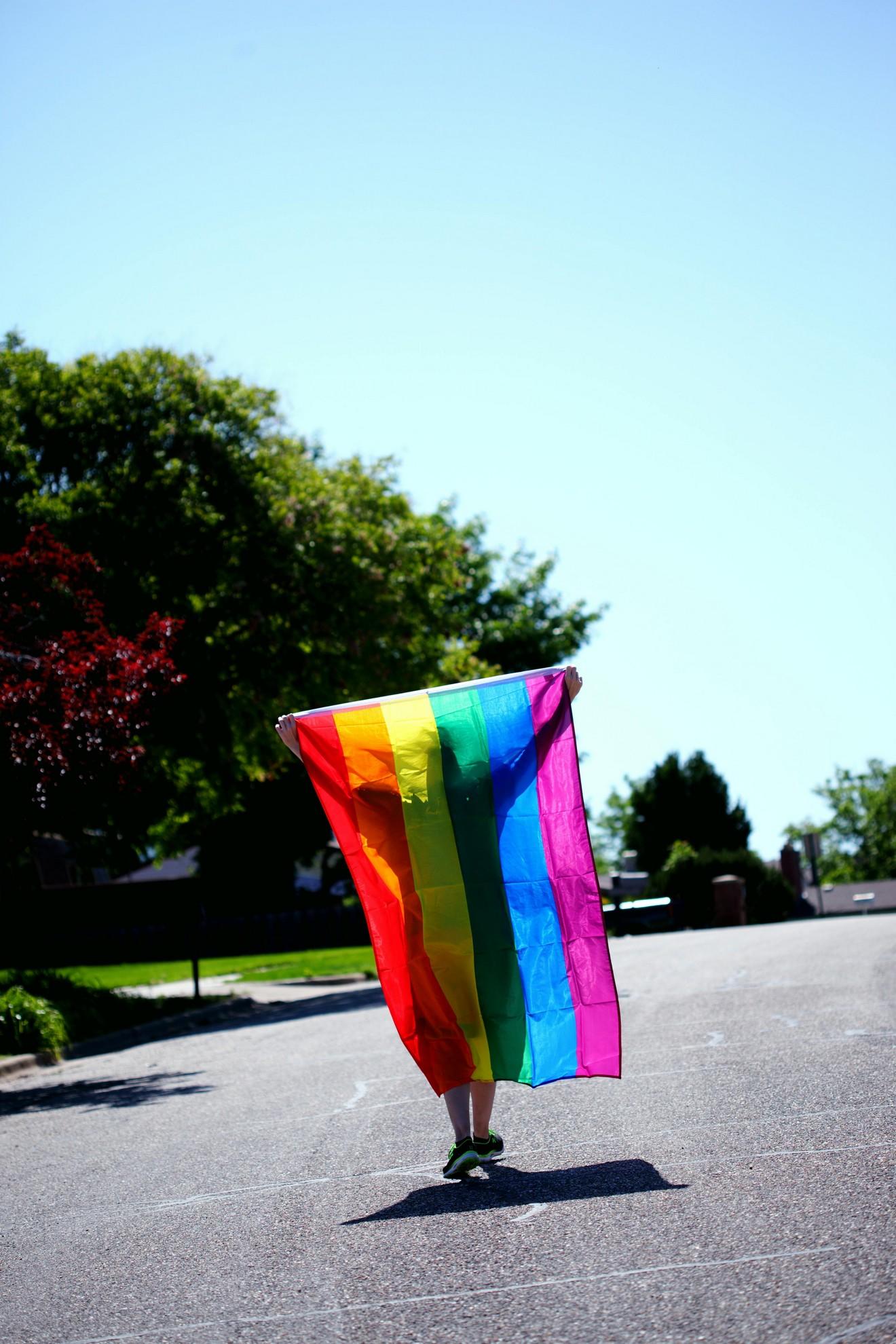Une personne dans la rue brandissant le drapeau de la gaypride.
