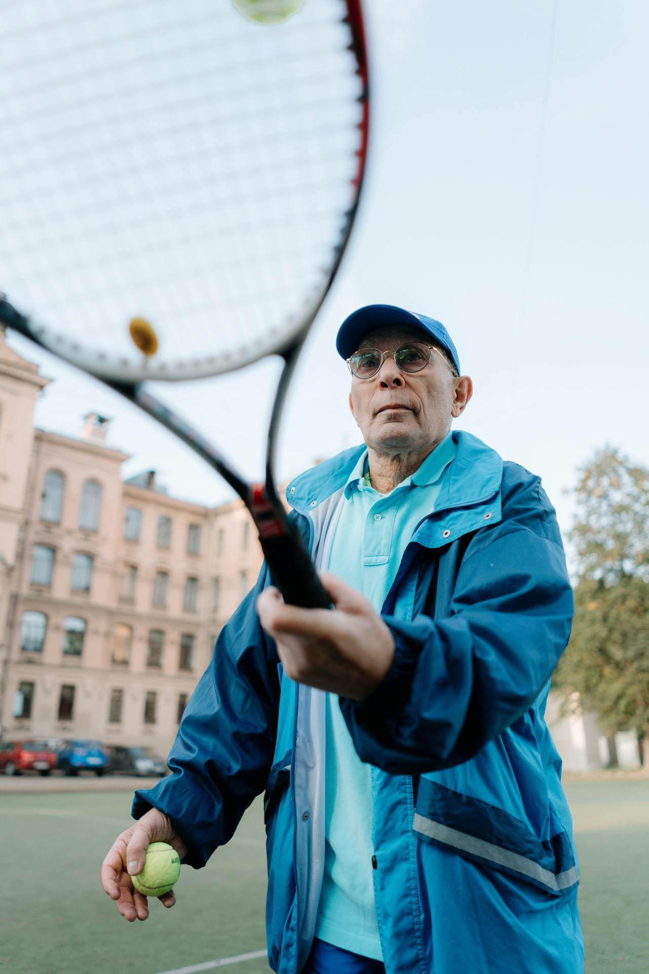 Homme d'une soixantaine d'années qui se prépare à lancer une balle de tennis avec sa raquette.