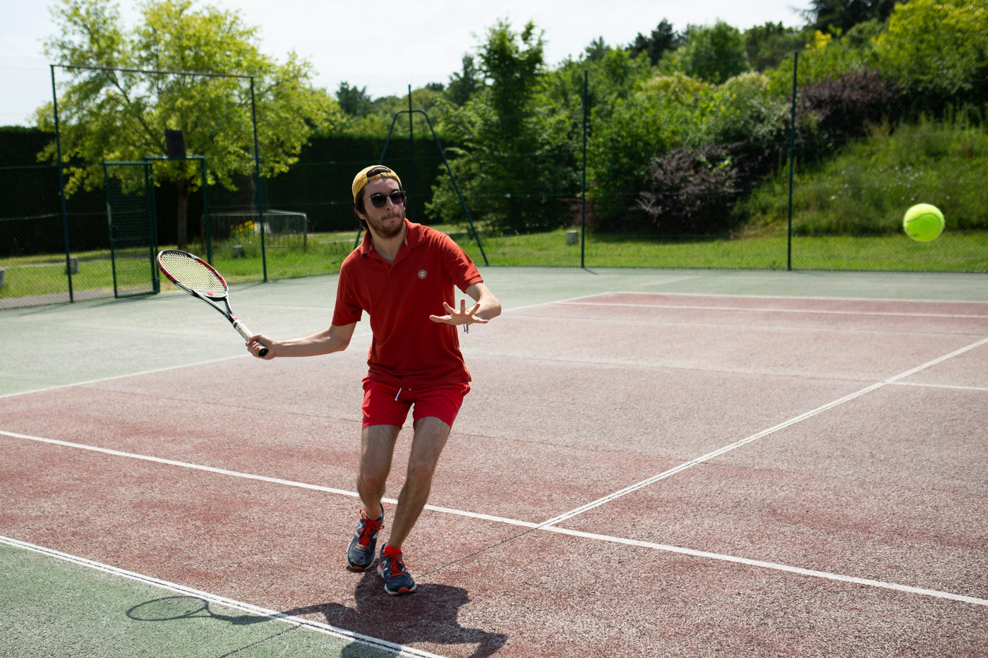Jeune homme recevant une balle de tennis sur un court en dur en extérieur.
