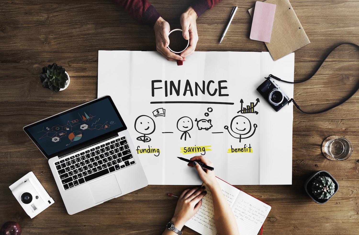 Un ordinateur est posé sur une table avec une feuille sur laquelle est écrit "finance".