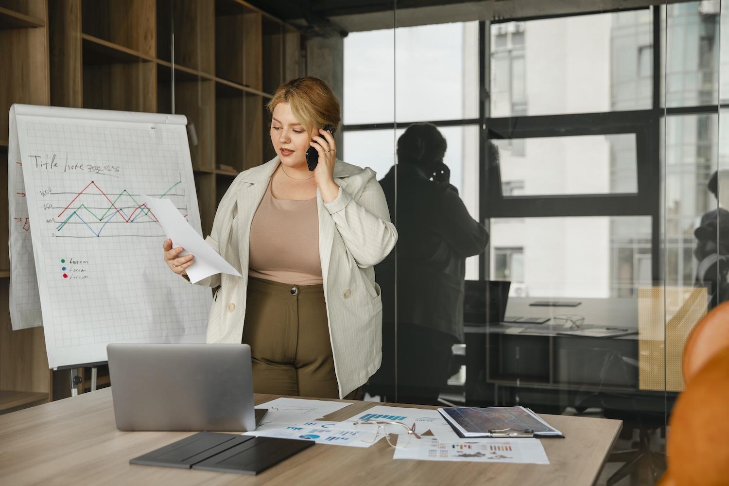 Une femme est dans un bureau avec un tableau derrière contenant des graphiques.