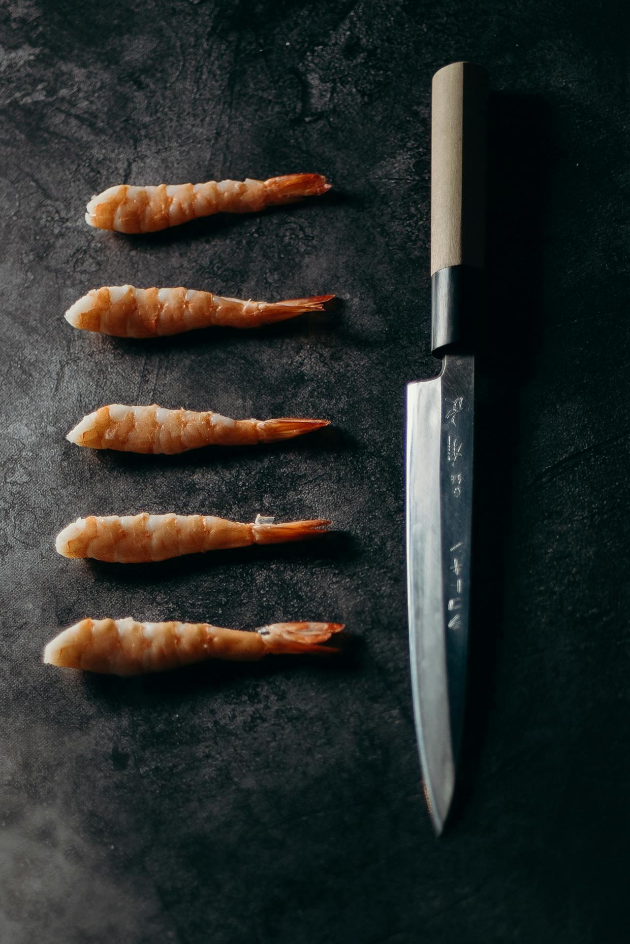 Crevettes alignées à côté d'un couteau japonais.