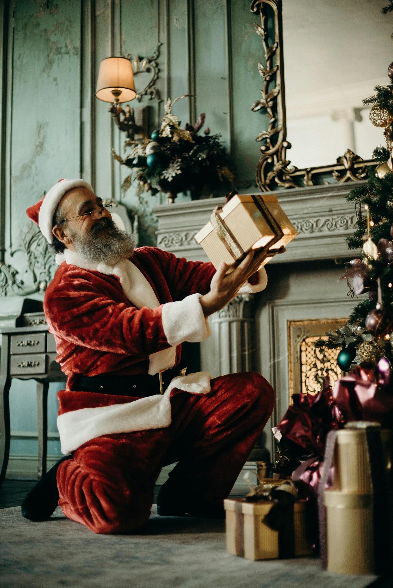 Le père Noël en train de déposer des cadeaux au pied du sapin.