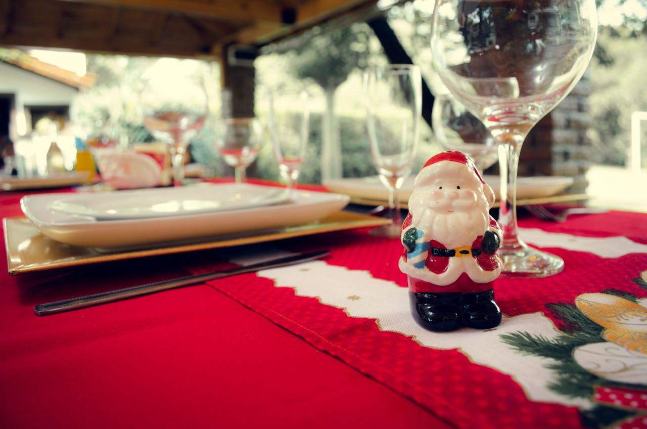 Une table de Noël dressée avec une nappe rouge et un père Noël au premier plan. 