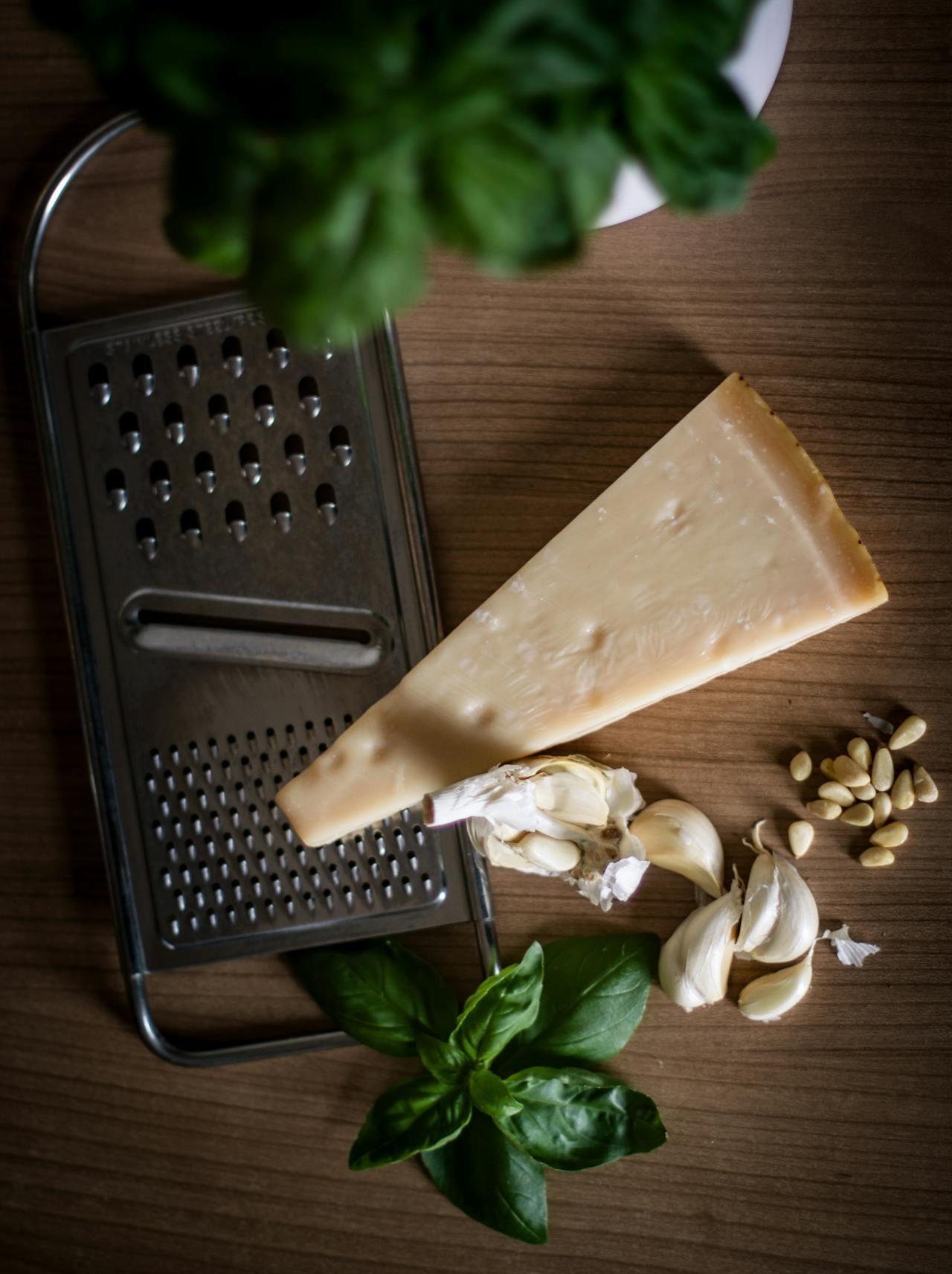 Vue d'en haut : râpe à fromage, parmesan, gousses d'ail, pignons de pin et basilic pour faire du pesto maison