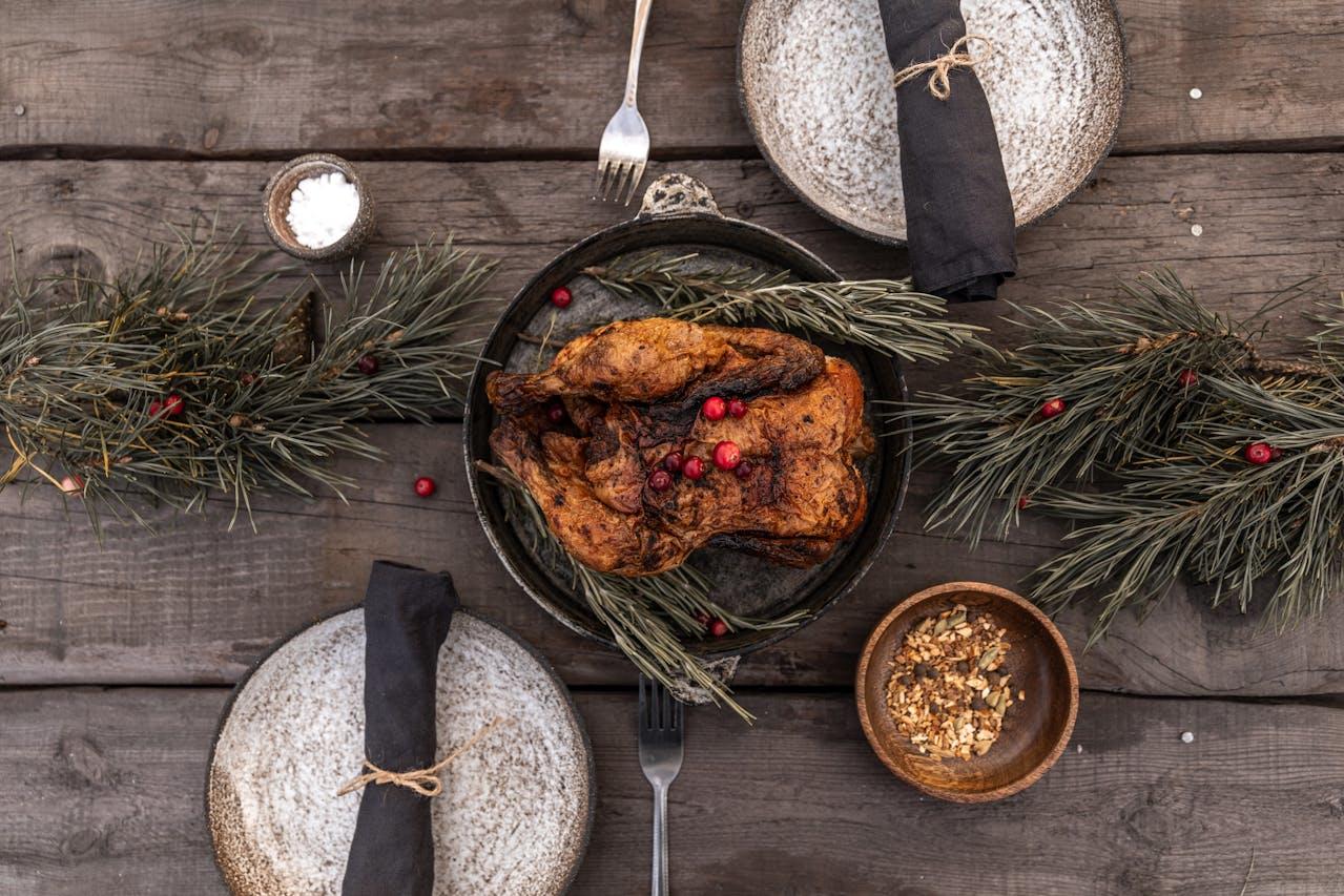 Vue d'en haut : poulet rôti posé sur une table avec des branches de sapin et des assiettes.