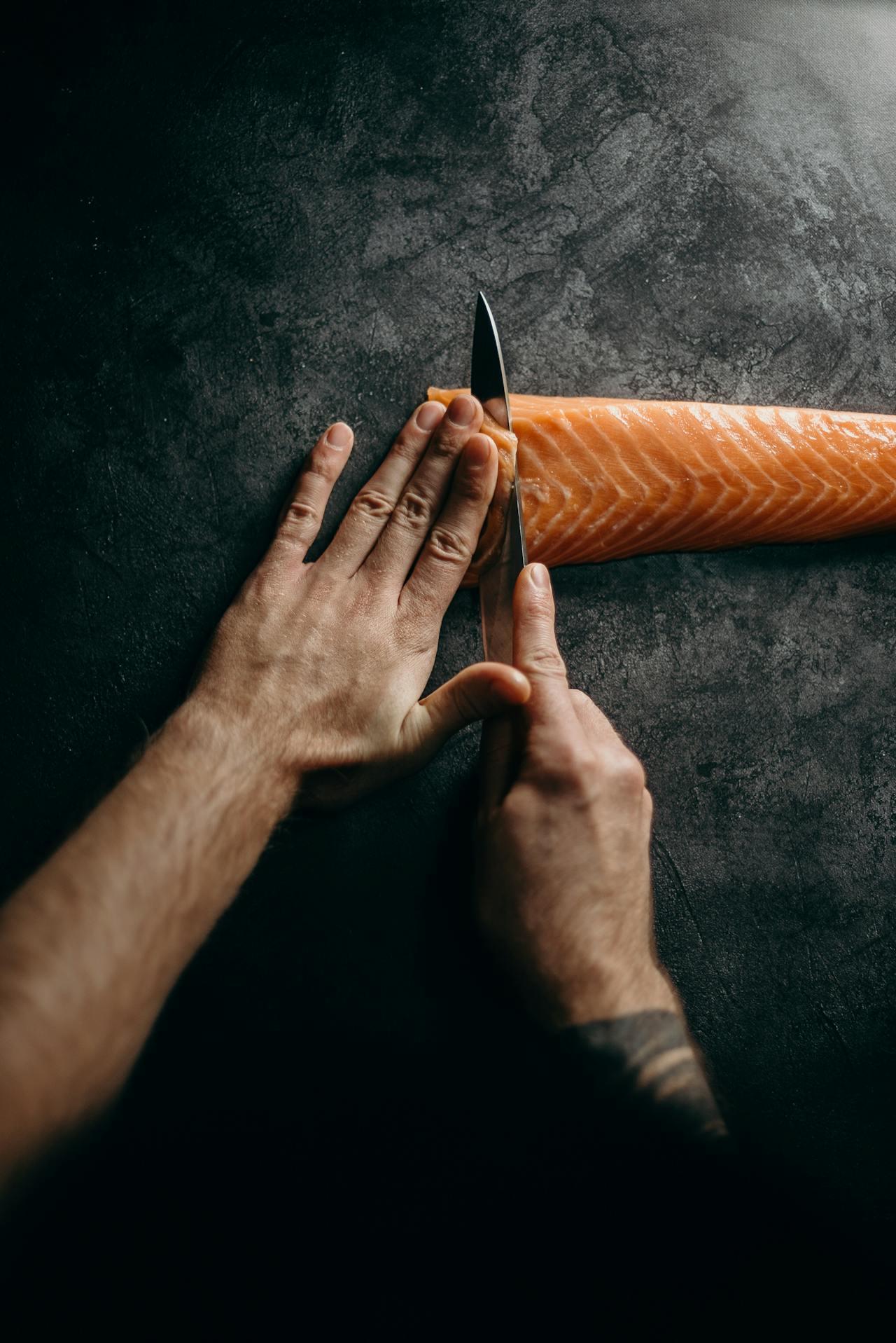 Mains d'un homme découpant du saumon cru en fines tranches. 