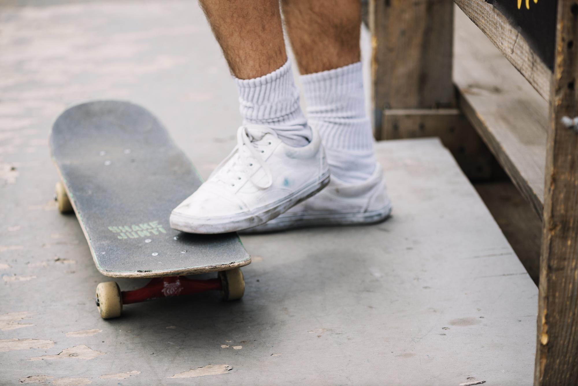 Un skateur avec des chaussures blanches a posé son pied sur sa planche de skate.