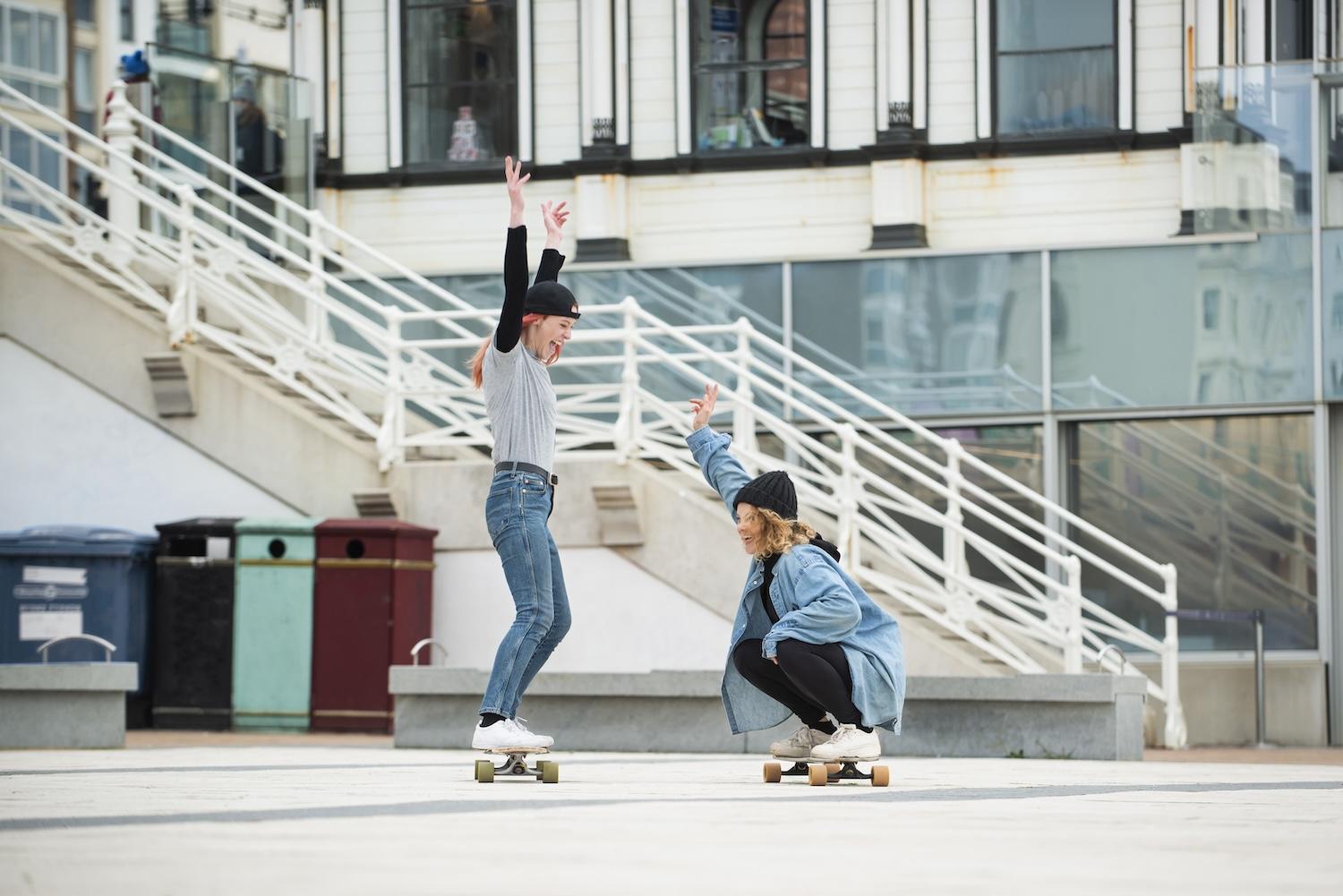 Deux jeunes femmes font du skate dans la rue.