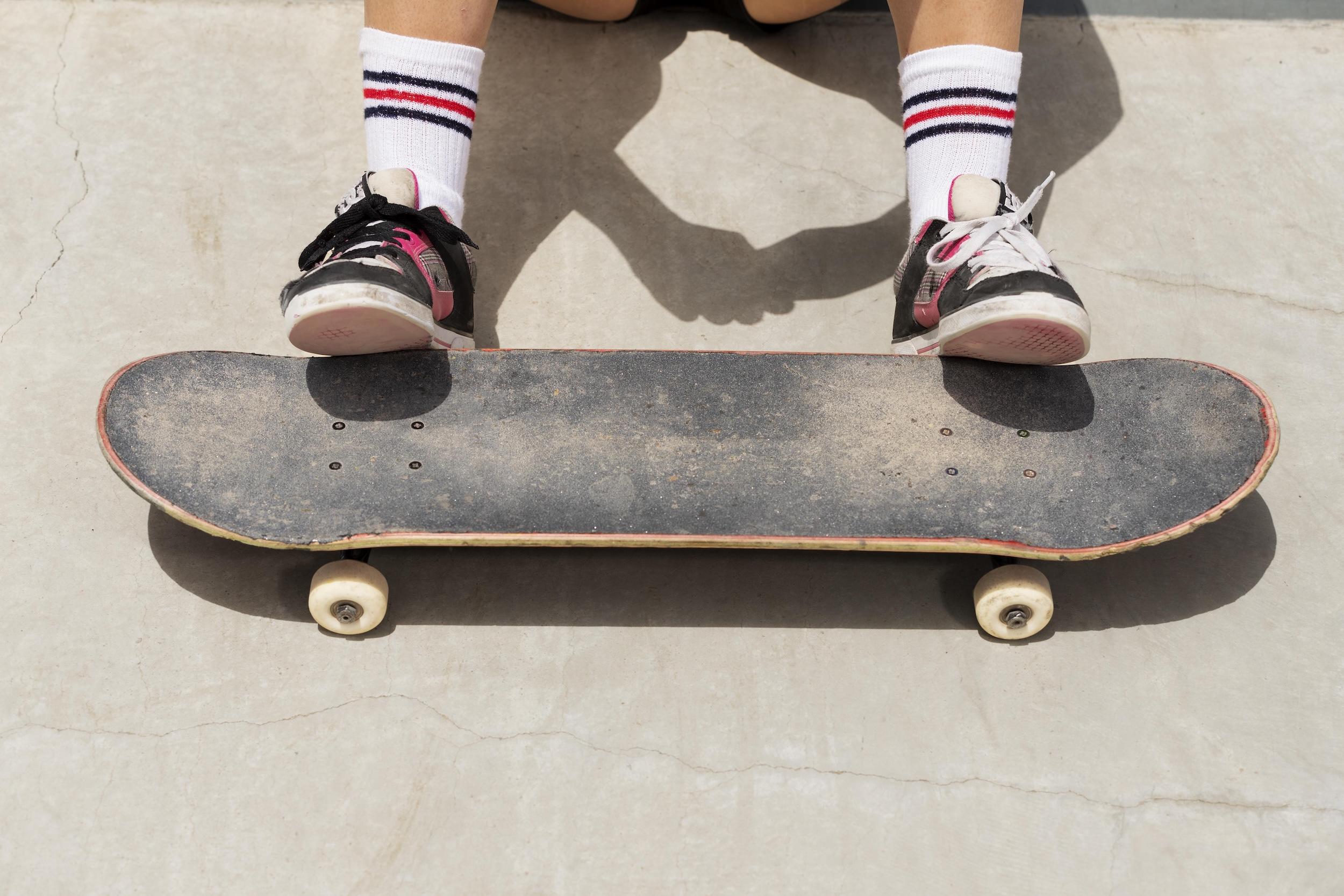 Une planche de skate avec les pieds d'un skateur posés dessus.