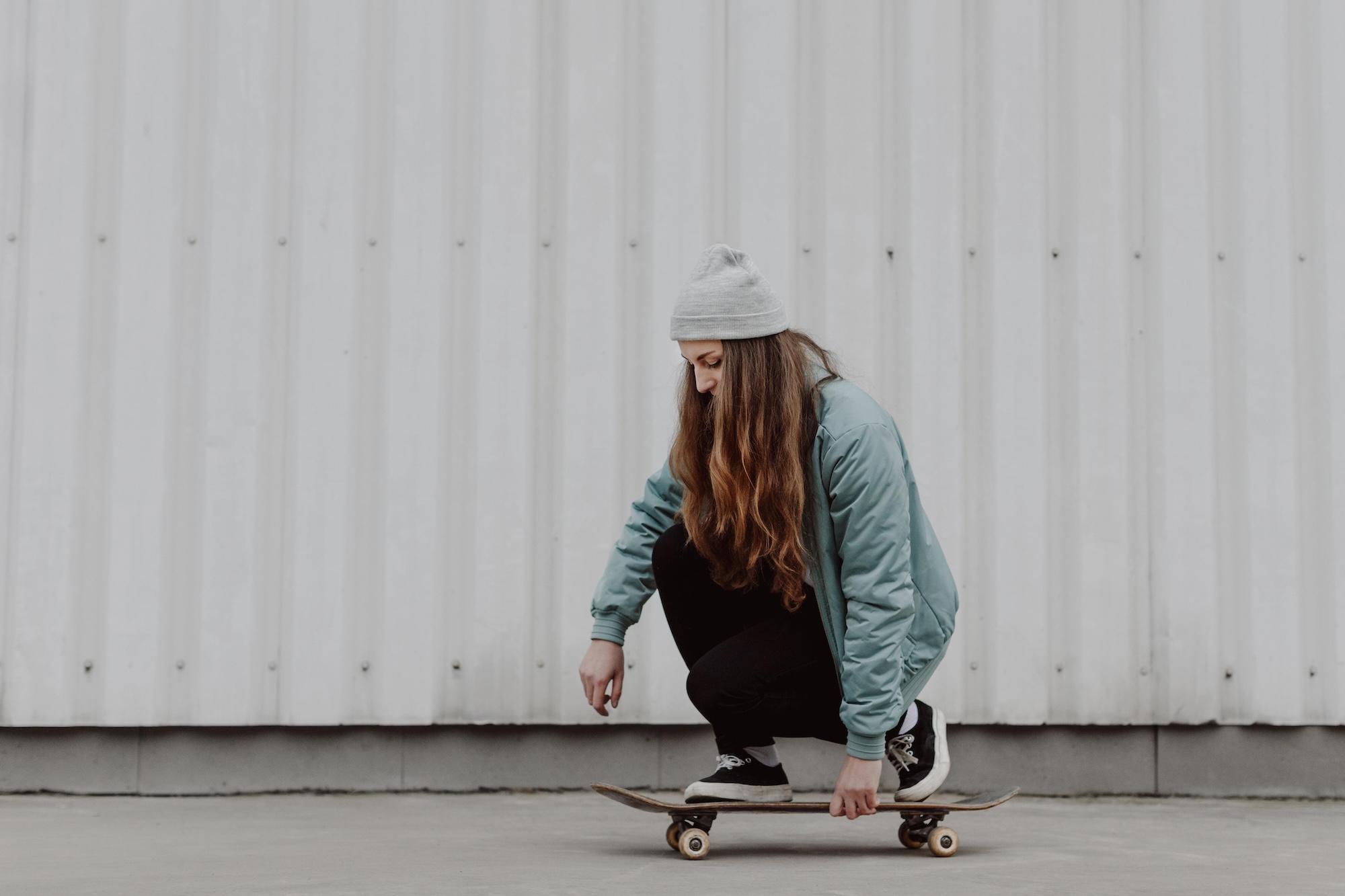 Une jeune femme est accroupie sur un skate en ville.