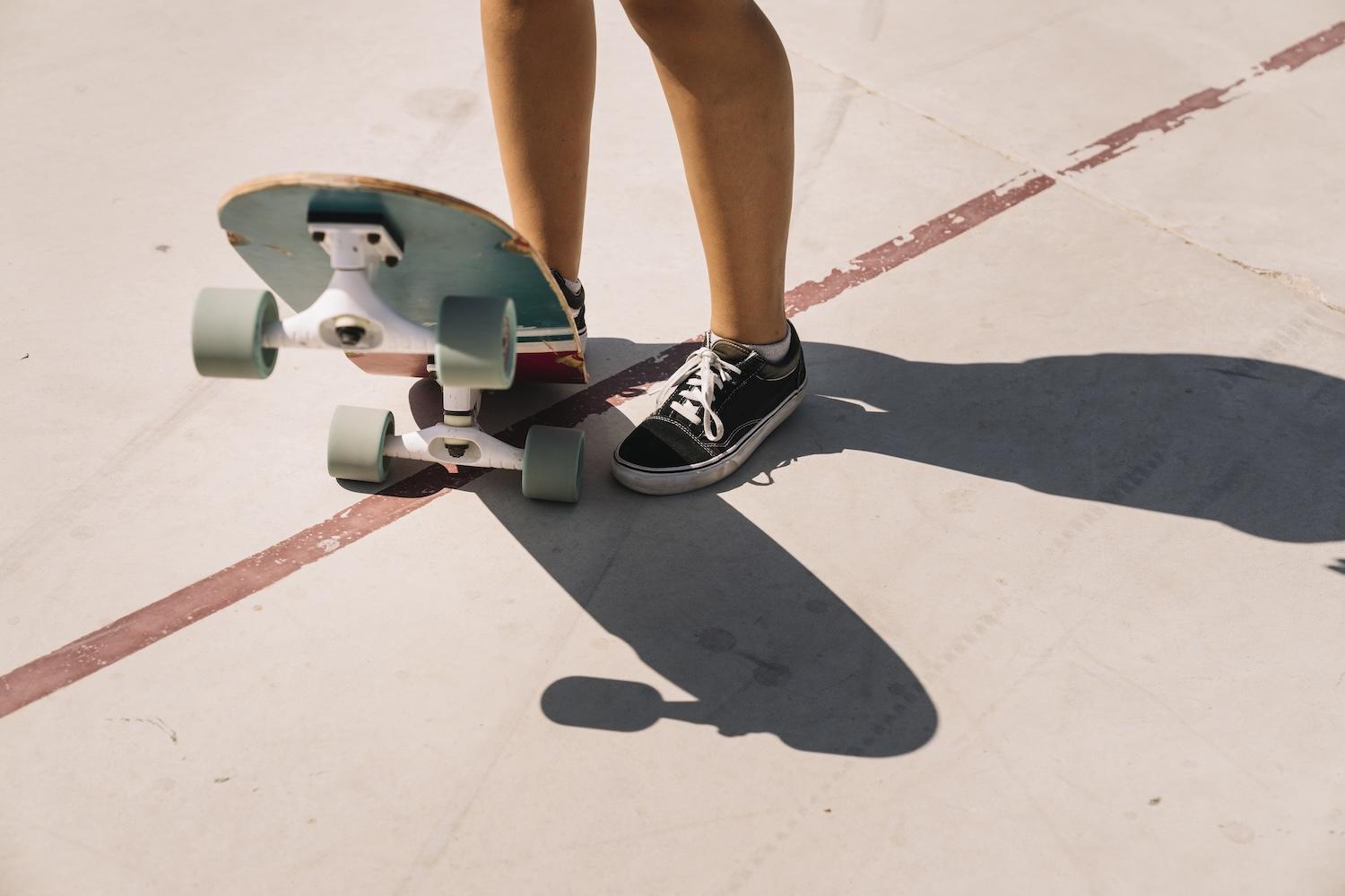 Un skateur avec des baskets noires tient un skate avec son pied.