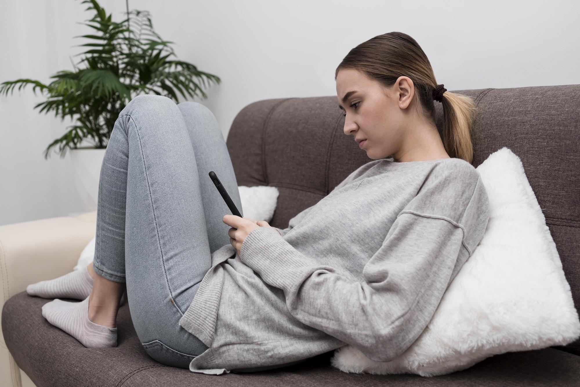 Une jeune femme est assise sur le canapé et regarde son smartphone