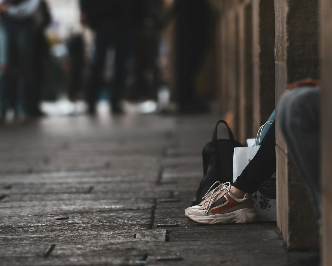 Photo de rue floue avec seulement les jambes d'une femme assise par terre qui dépassent d'un bloc de mur. 
