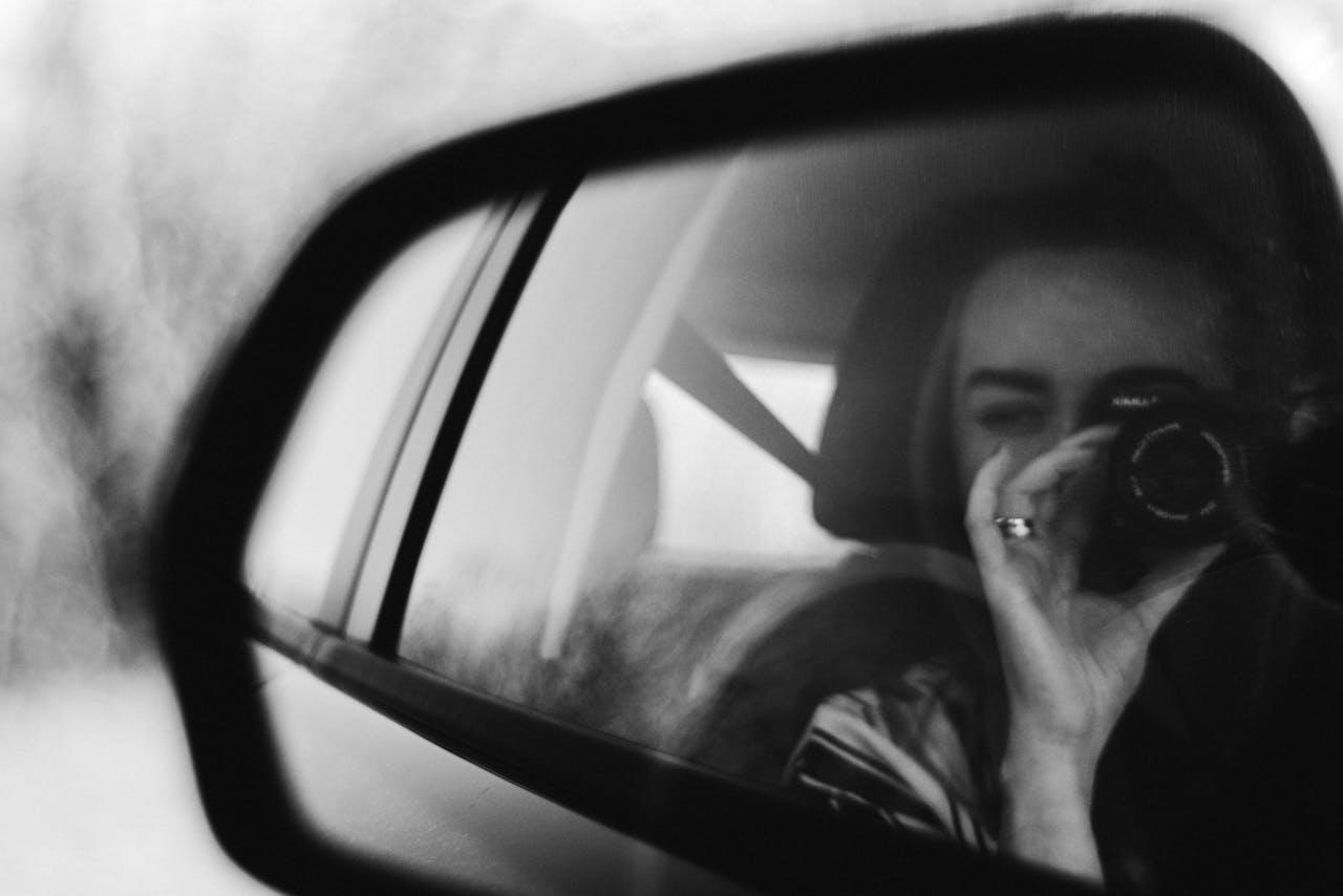 Jeune femme se prenant en photo dans le rétroviseur d'une voiture. 