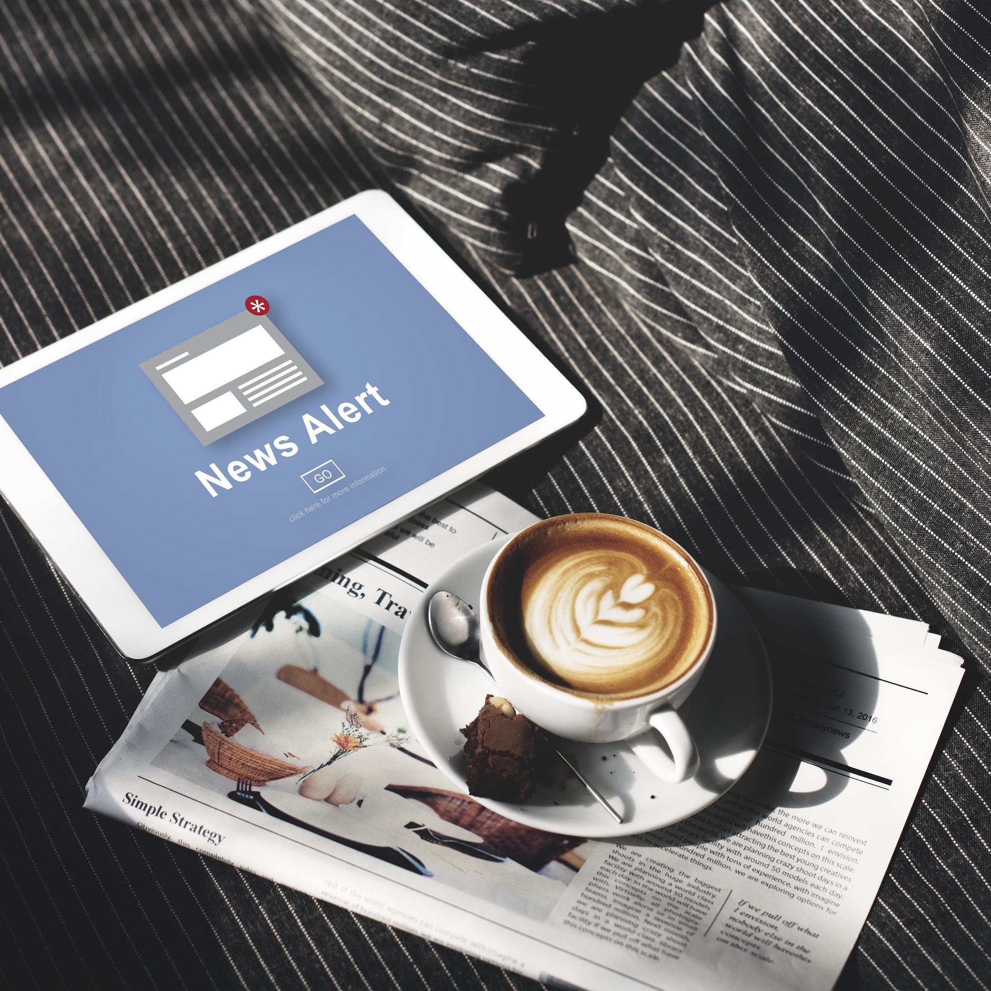 Une tablette est posée à côté d'un journal et d'un café