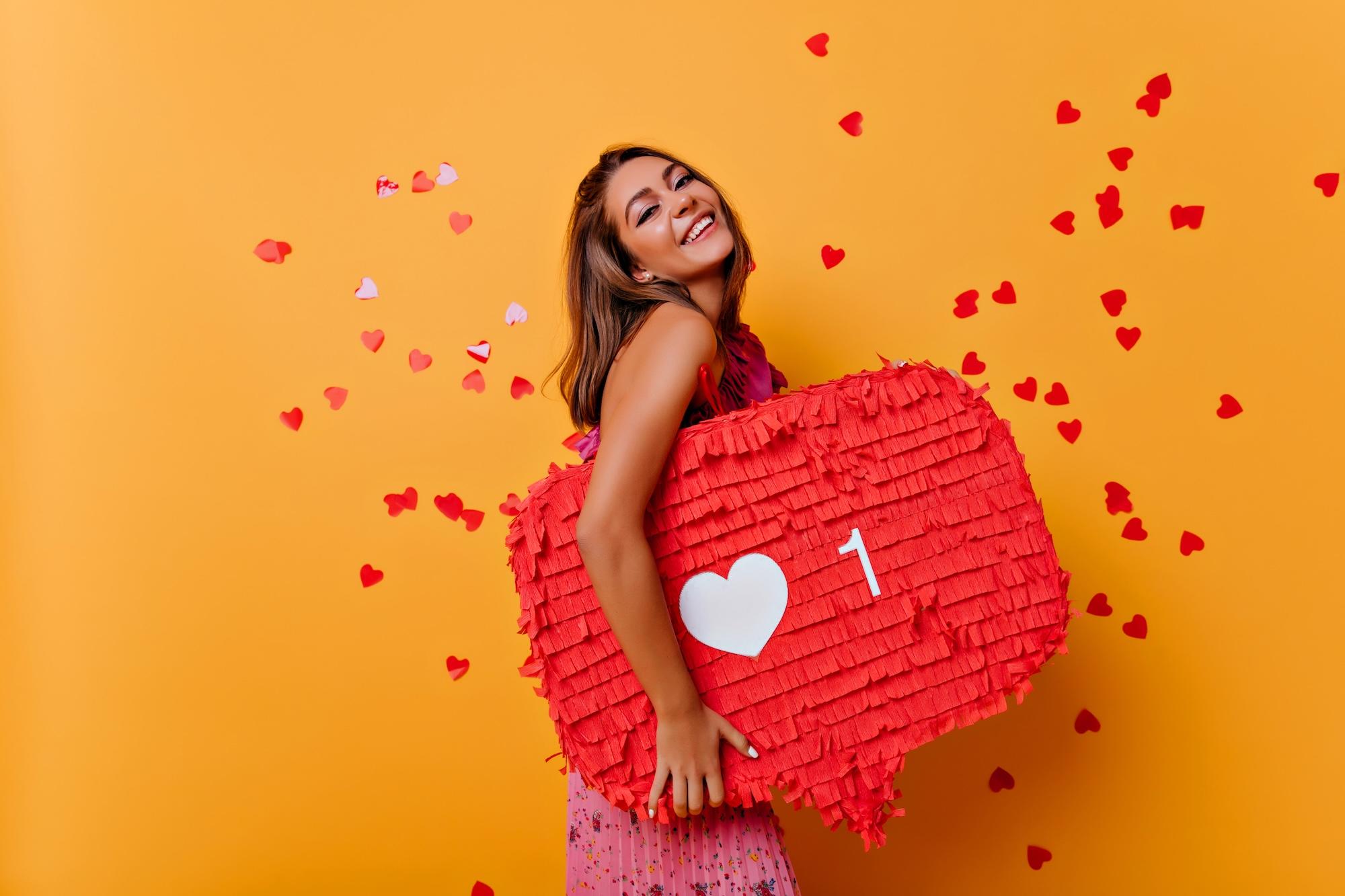 Une jeune femme souriante porte un like rouge en papier dans ses bras.