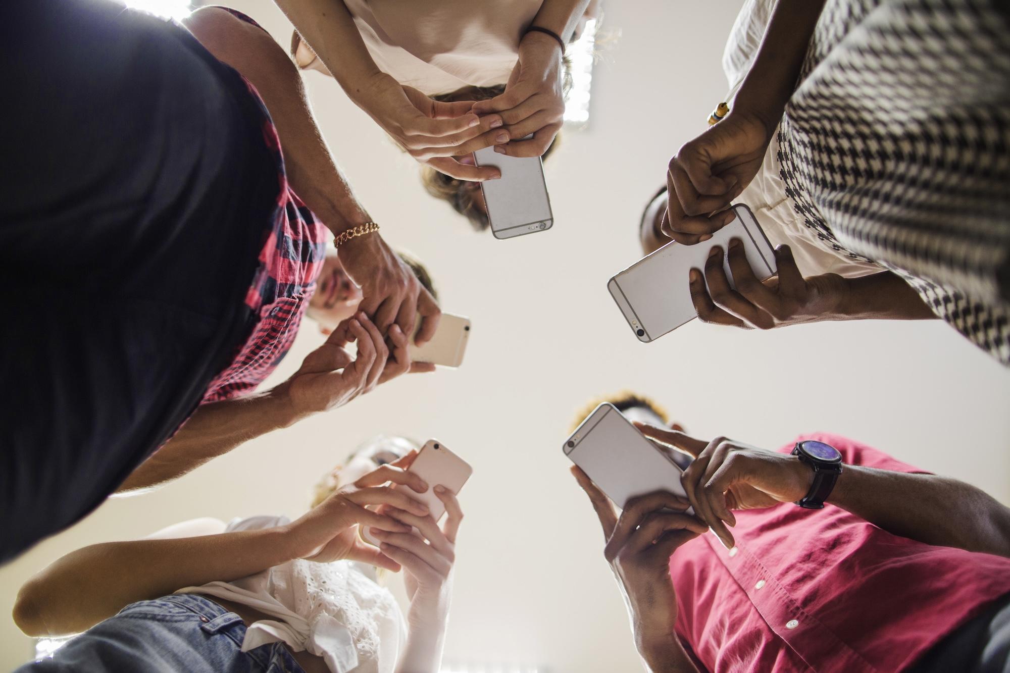 Des personnes vue d'en bas tiennent leur smartphone dans les mains.