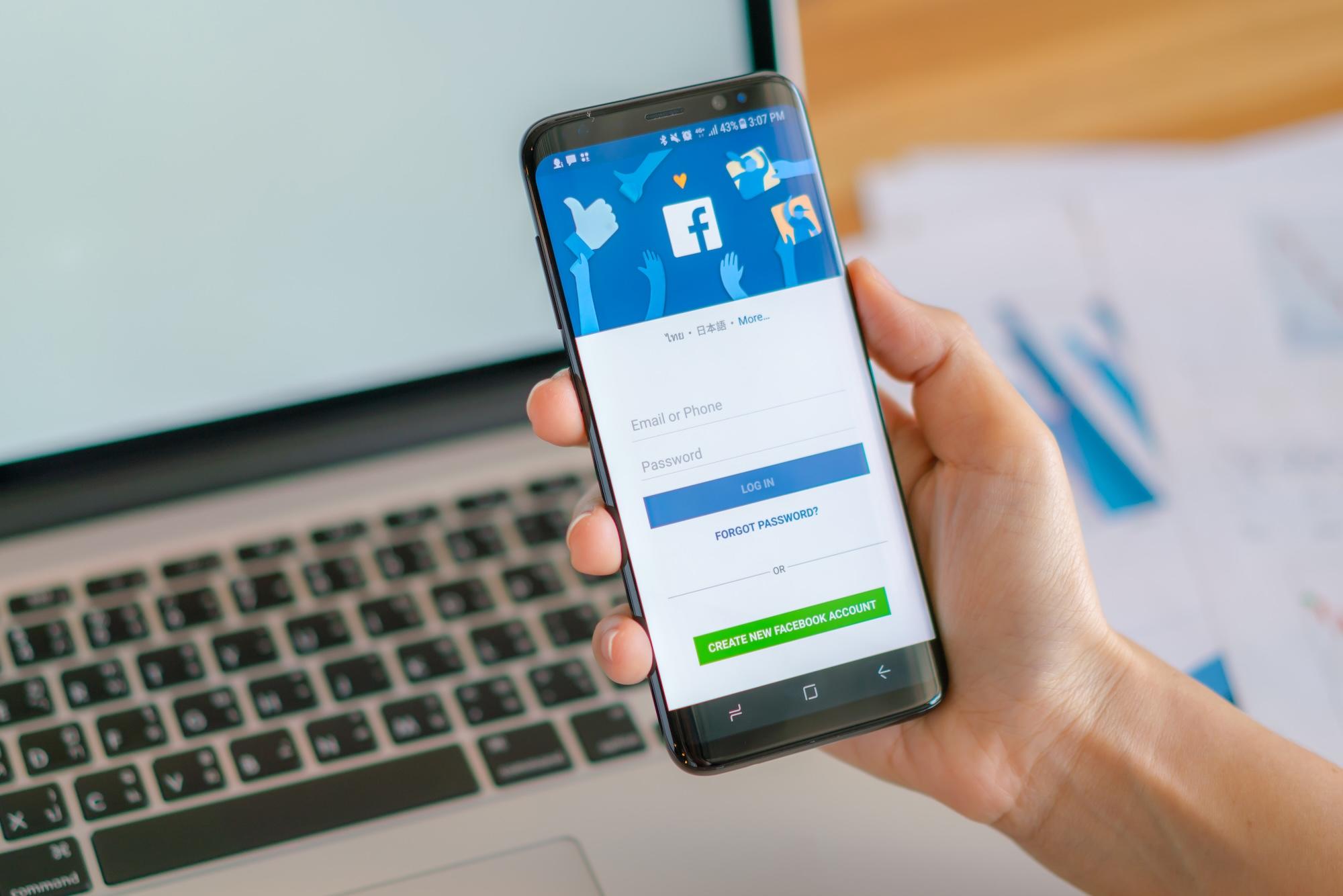 Main tenant un Samsung S8 avec une application mobile pour Facebook sur l'écran