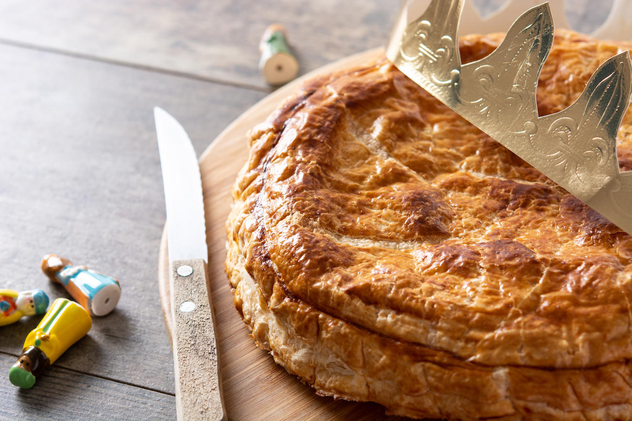 Galette posée sur une table avec une couronne dessus et trois fèves à côté.