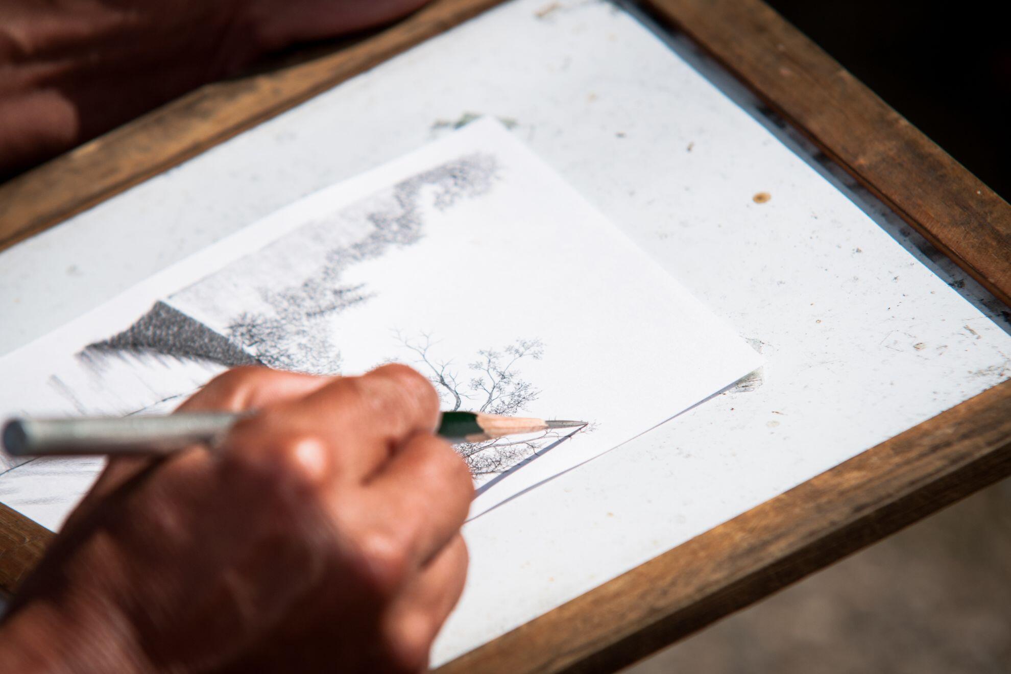 Une personne en train de dessiner au crayon gris.