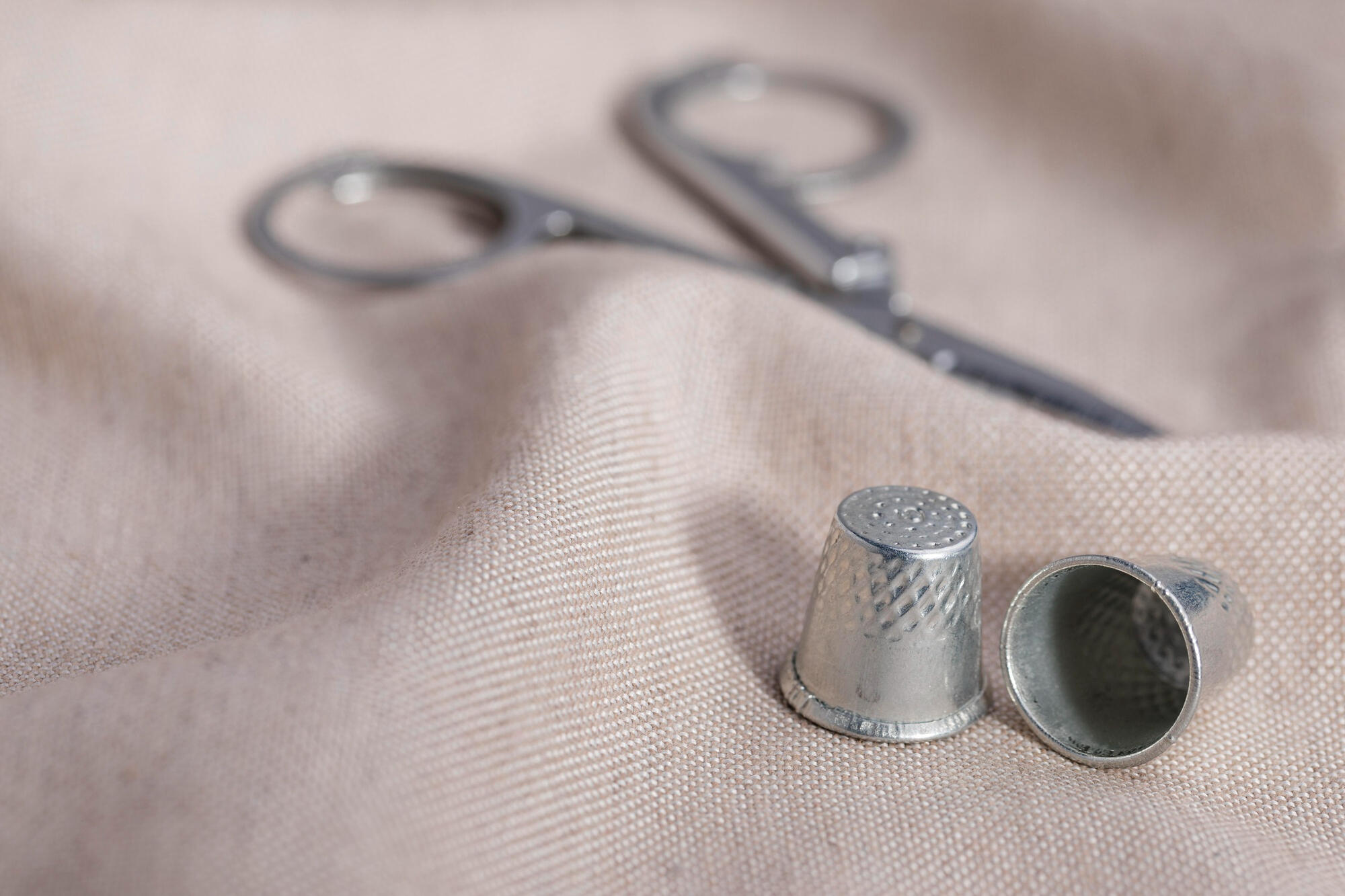Des dés à coudre avec une paire de ciseaux sur un textile.