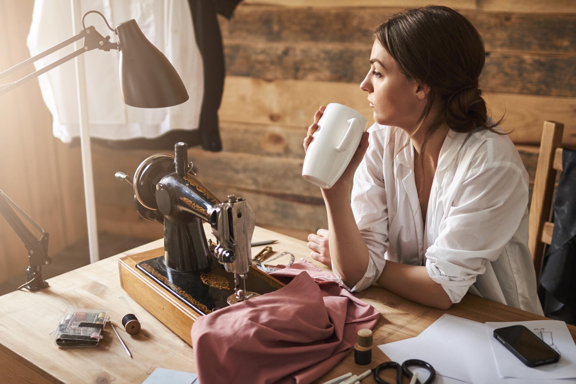 Une femme est en train de tenir une tasse devant sa machine à coudre