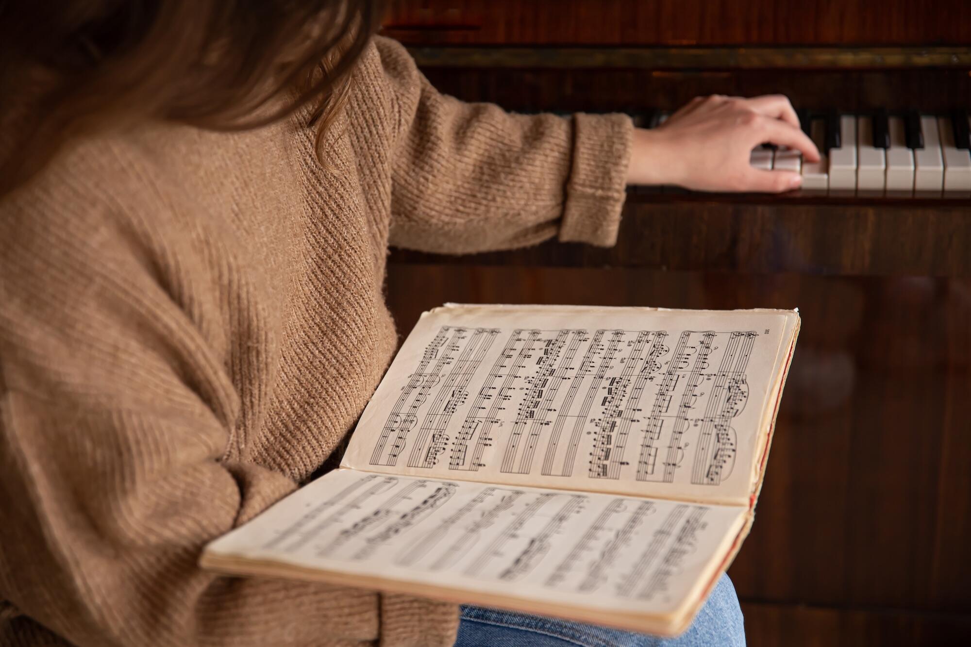 Une jeune femme tient une partition et joue du piano