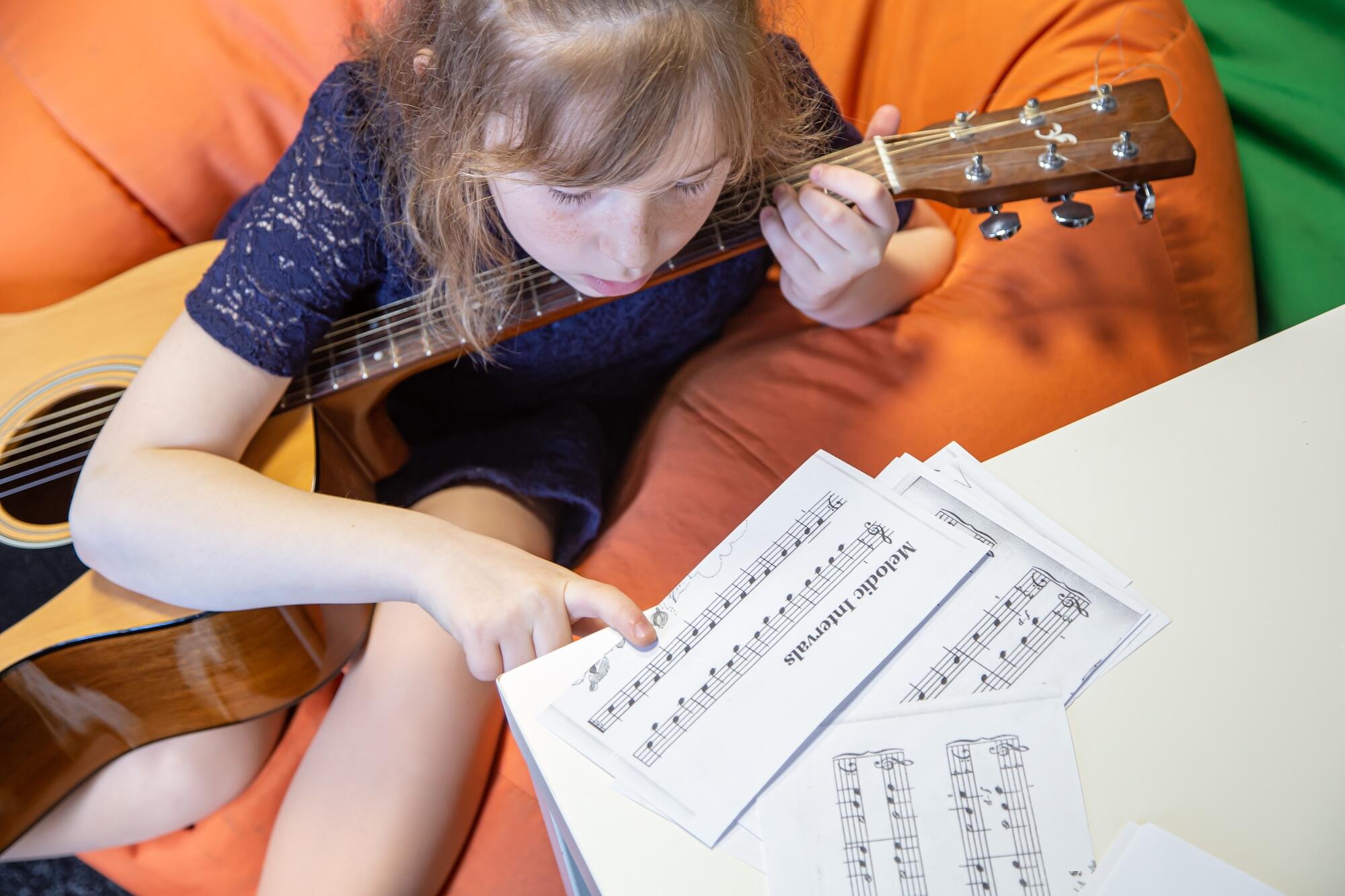 Une petite fille est en train d'apprendre le solfège avec une guitare.