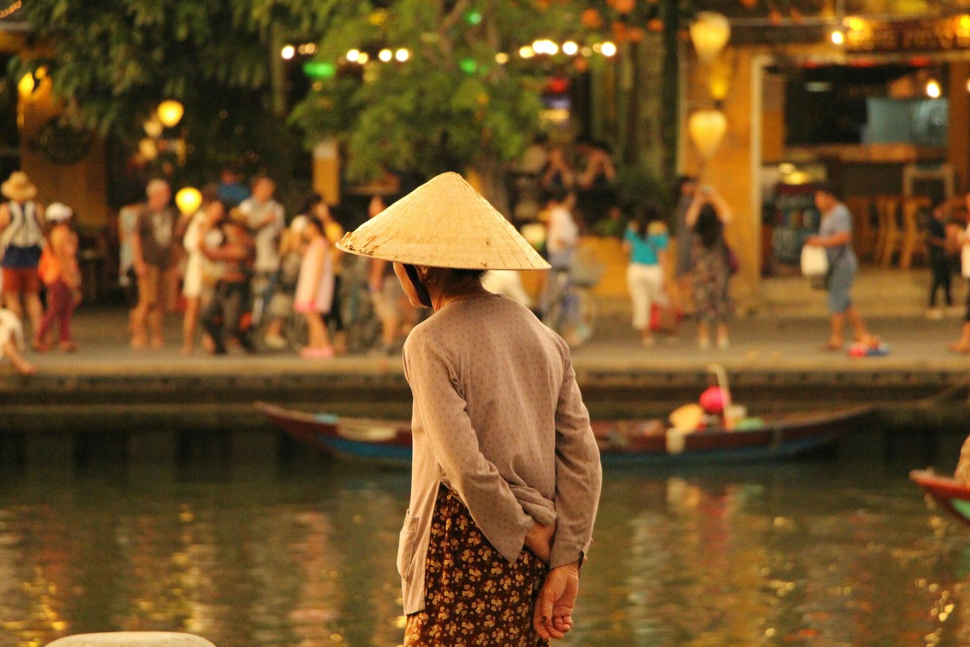 Femme vietnamienne vue de dos, devant un point d'eau, portant le chapeau traditionnel.