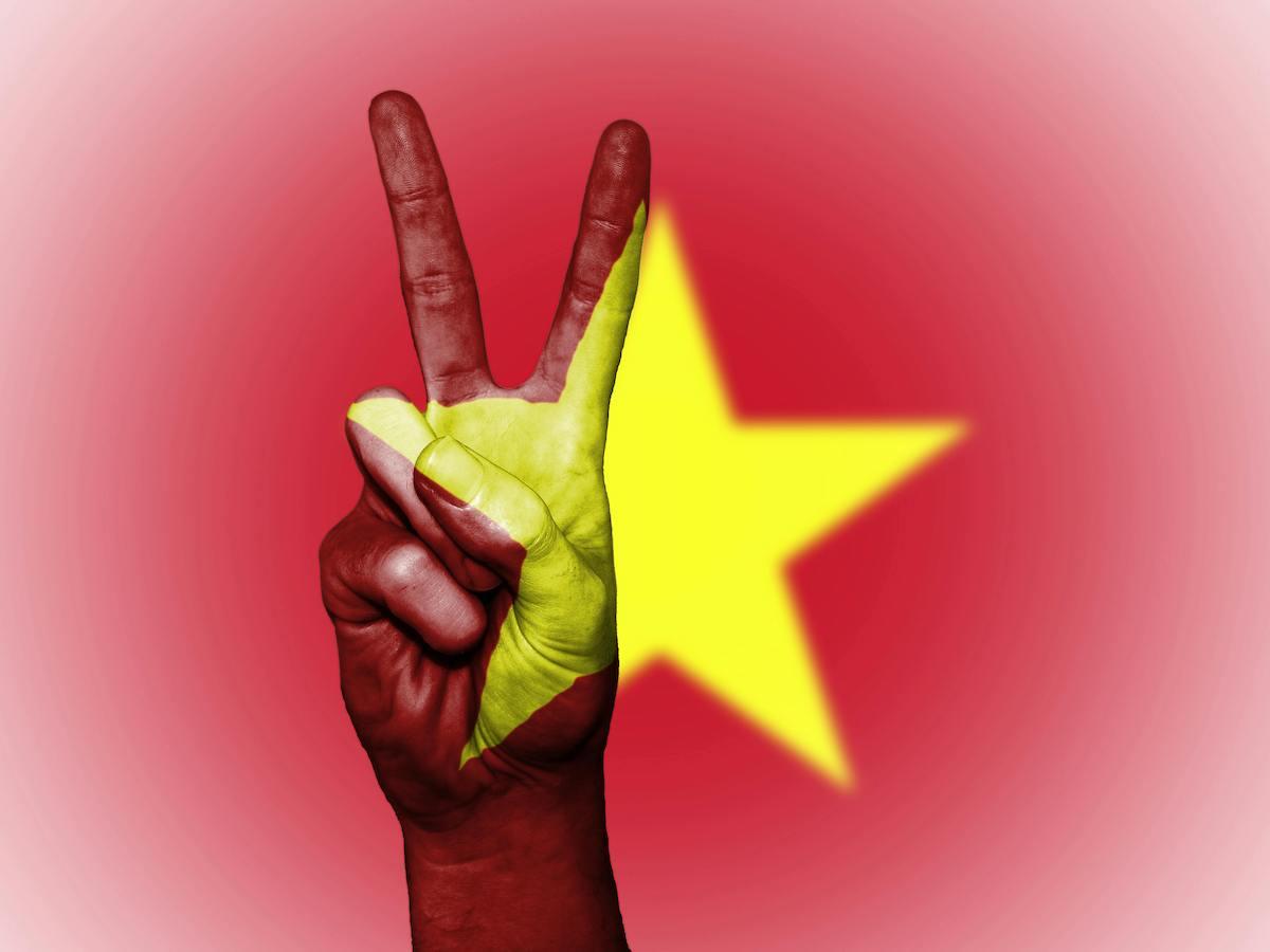Drapeau du Vietnam avec une main faisant le signe de la victoire devant. 