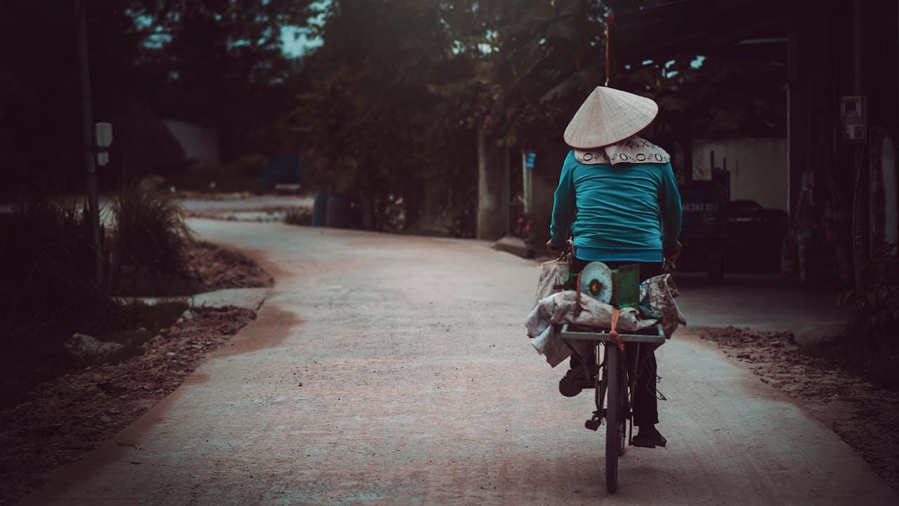 Vietnamien sur son vélo de dos sur une route au Vietnam avec un chapeau traditionnel sur la tête. 