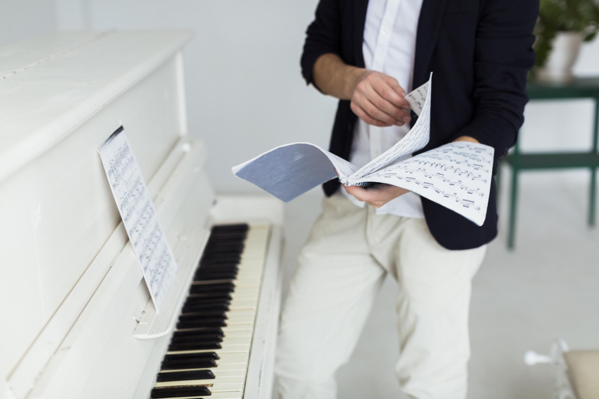 Un homme tournant les pages de partitions musicales près du piano à queue